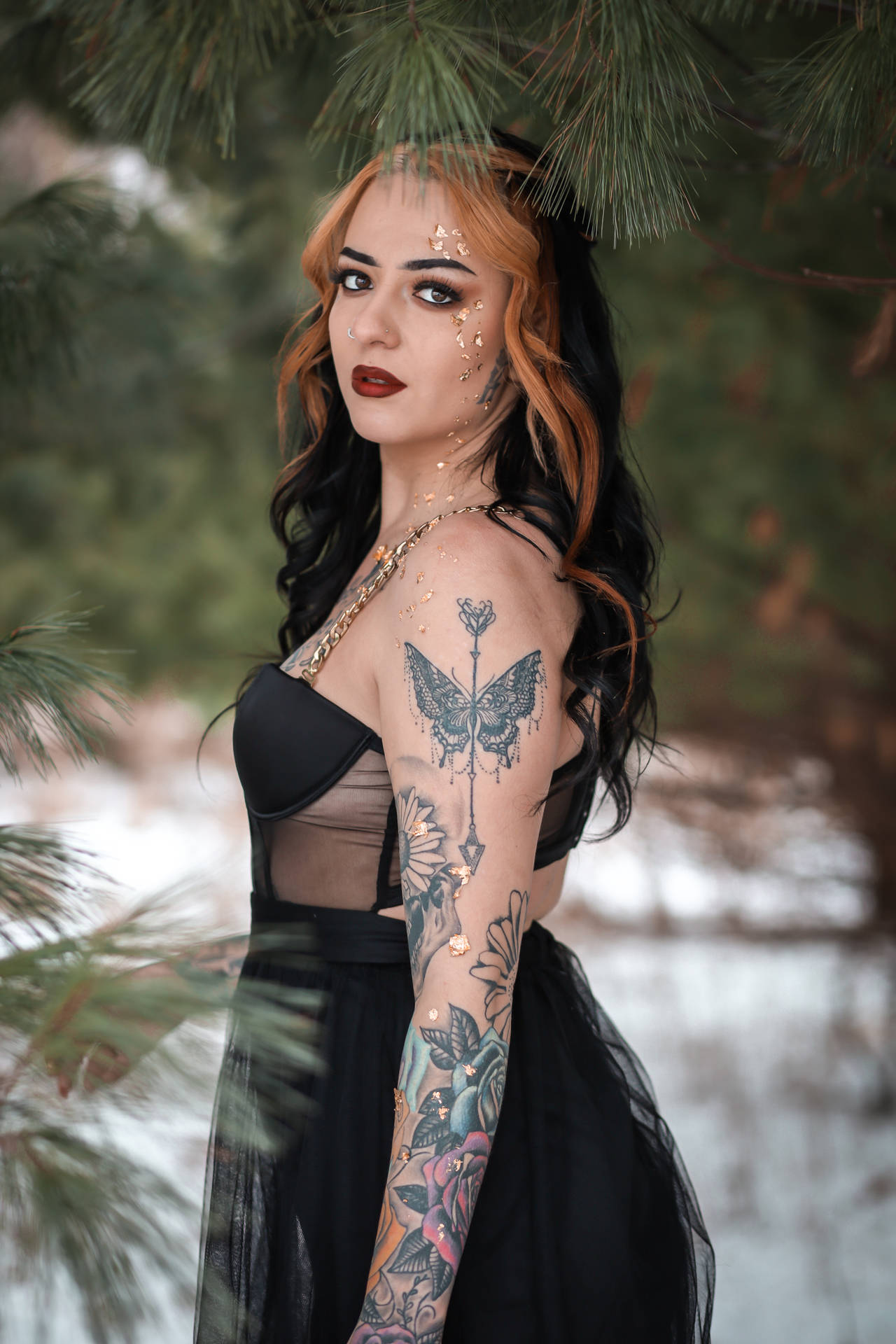 雪地森林中帶有紋身和閃粉穿著黑色連衣裙的女性