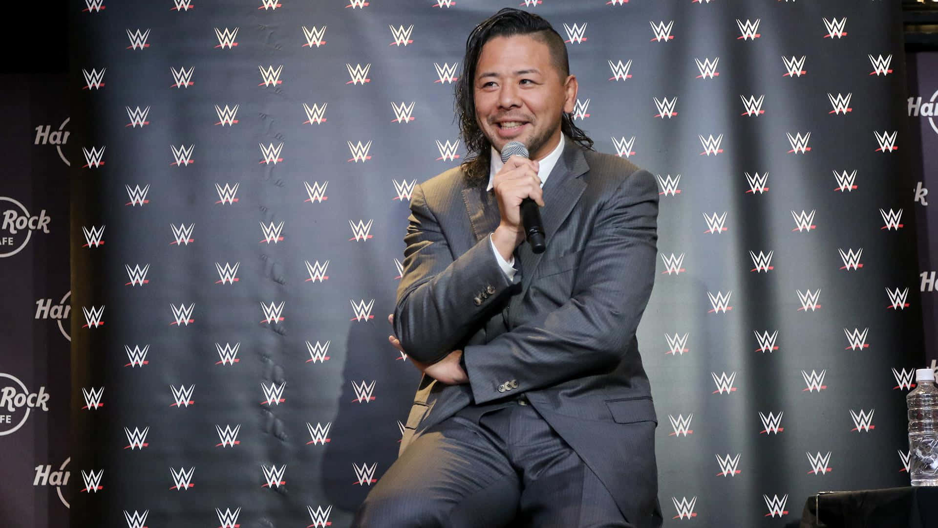 WWE活動中，身穿灰色西裝的摔角手微笑著手持麥克風。