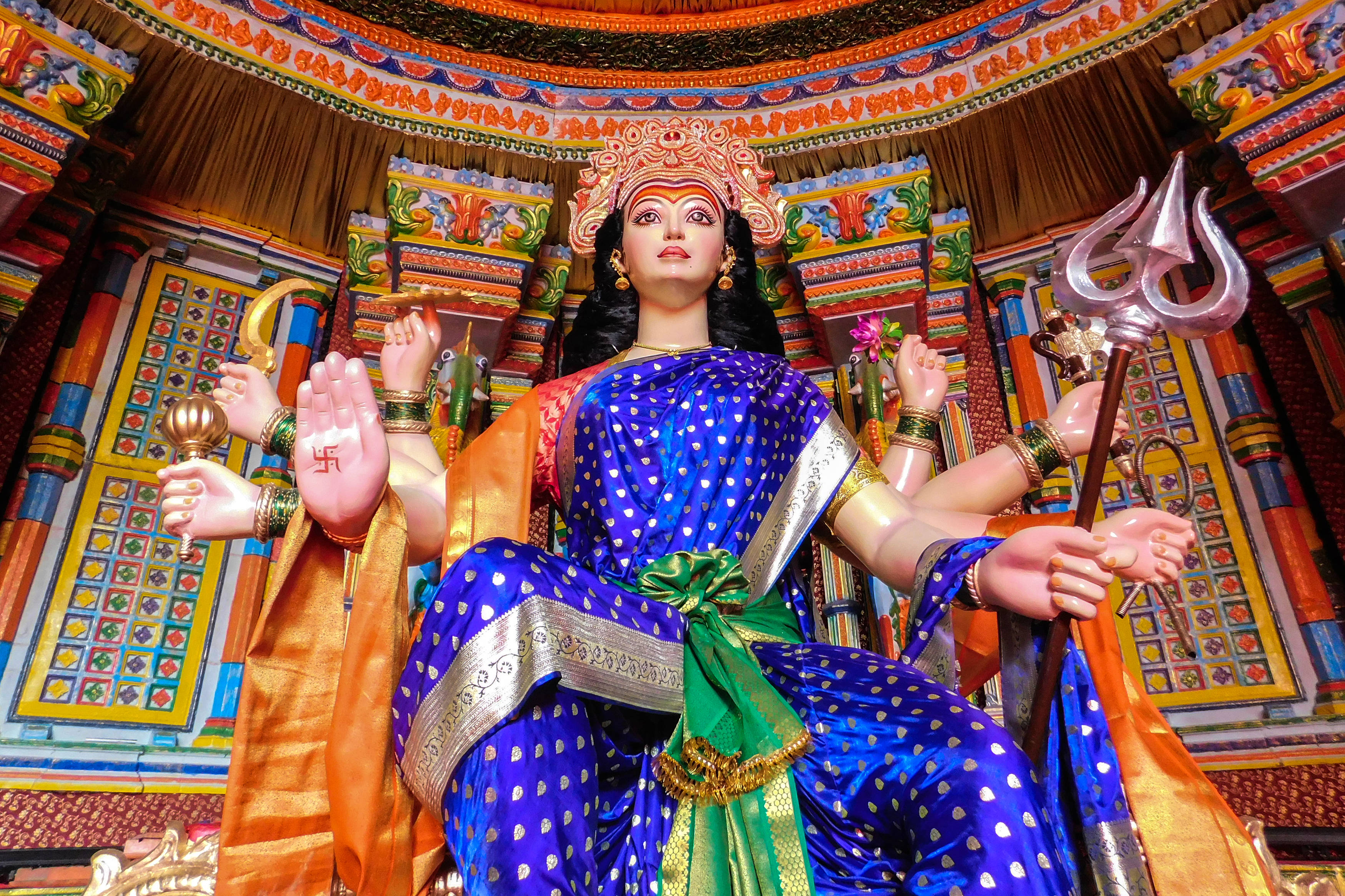 納瓦拉蒂持三叉戟 壁紙 — 一尊色彩鮮豔的印度教女神杜爾迦雕像，以藍色和金色裝飾，多臂手持武器，坐在裝飾華麗的寺廟神龕中。