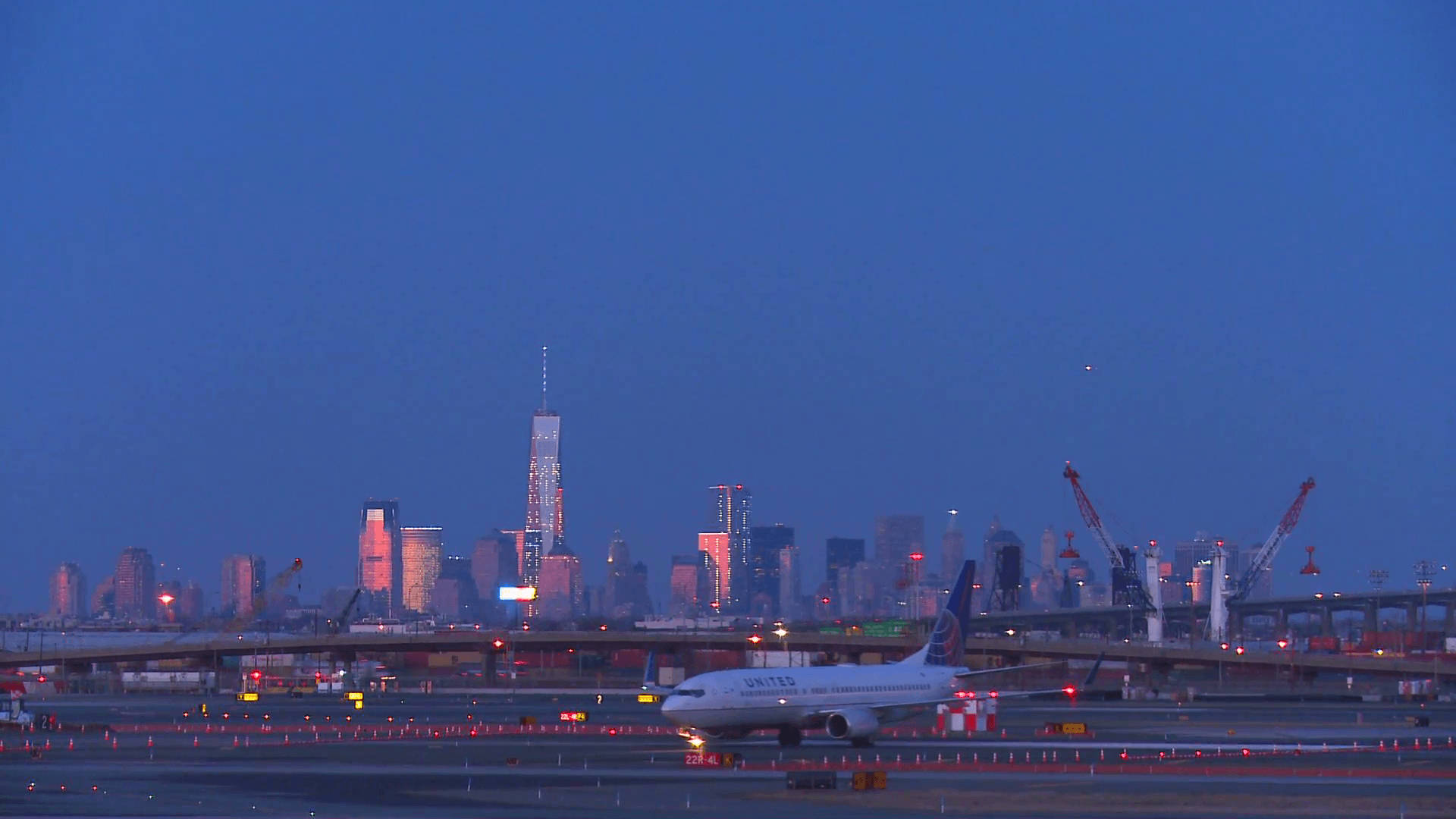 聯合航空飛機在跑道上，背景是黃昏時燈火通明的紐約市天際線。