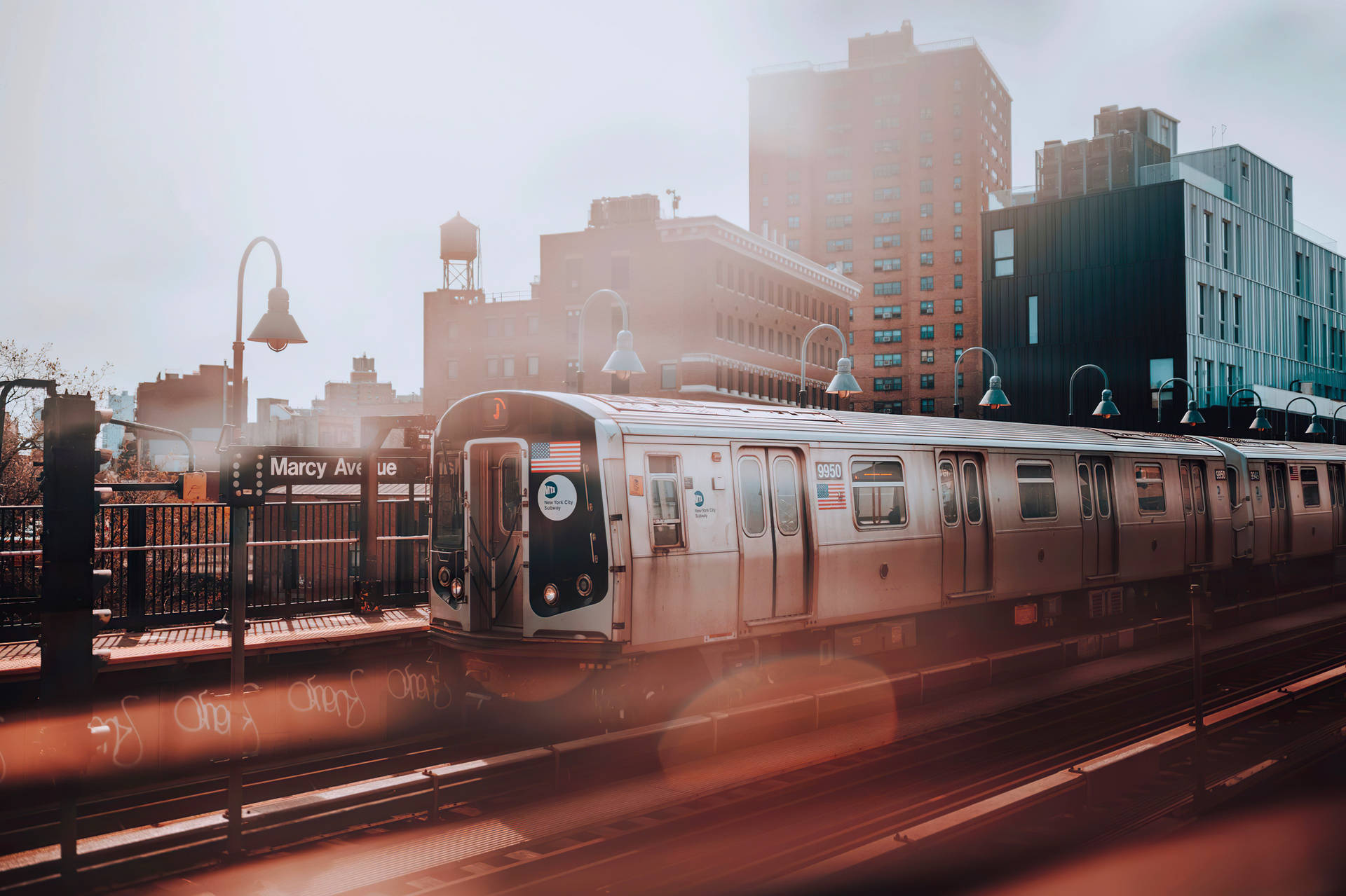Marcy Avenue 車站的銀色地鐵列車，金色夕陽餘暉和背景建築。