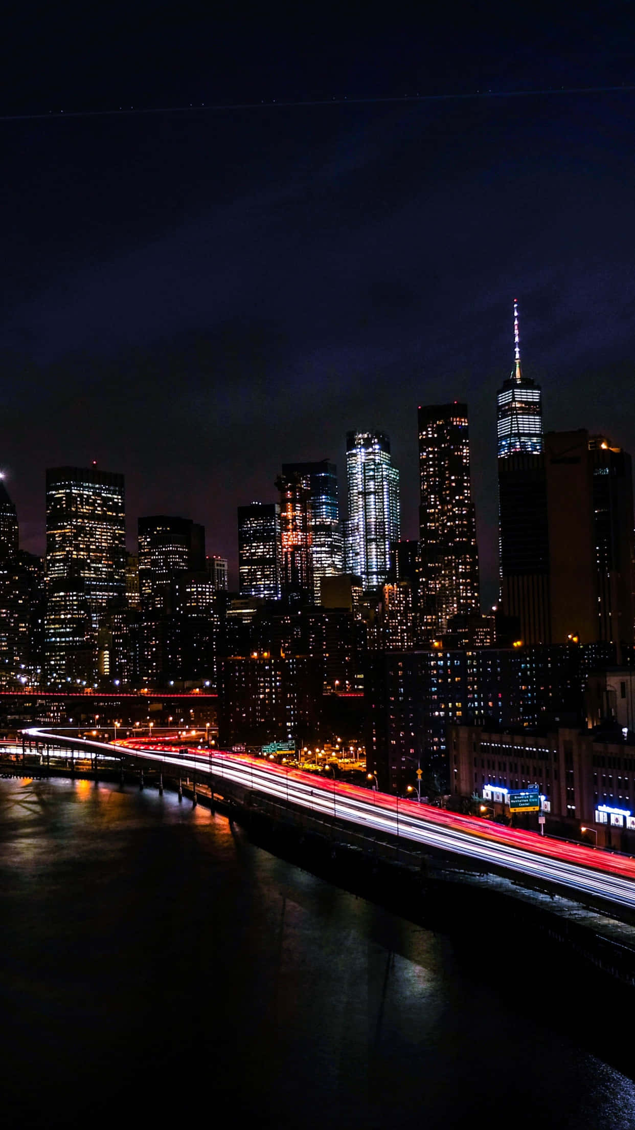 紐約夜景摩天大樓 壁紙 — 紐約充滿活力的夜景，閃爍的摩天大樓和在水面上劃過的紅色交通燈光。