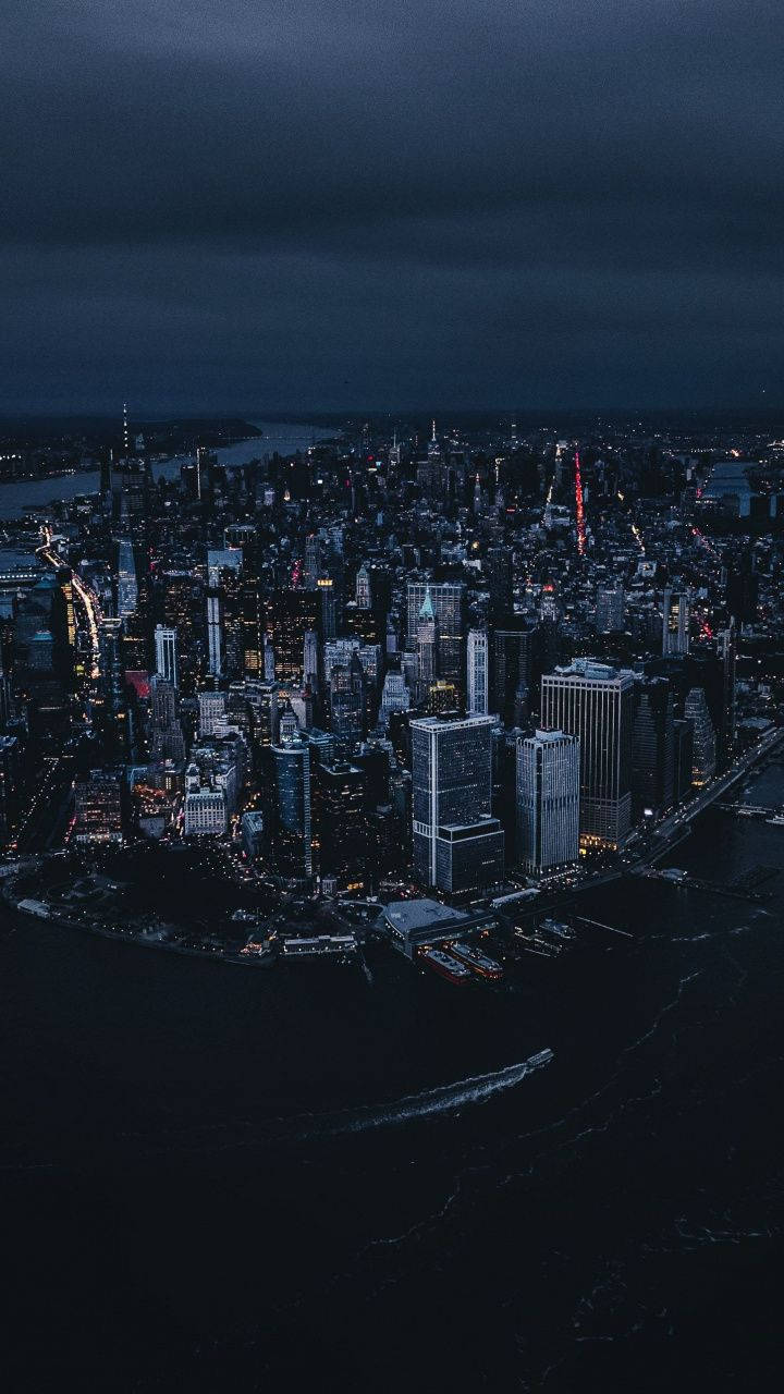 城市夜景鳥瞰圖，有燈火通明的摩天大樓和黑暗的水面。