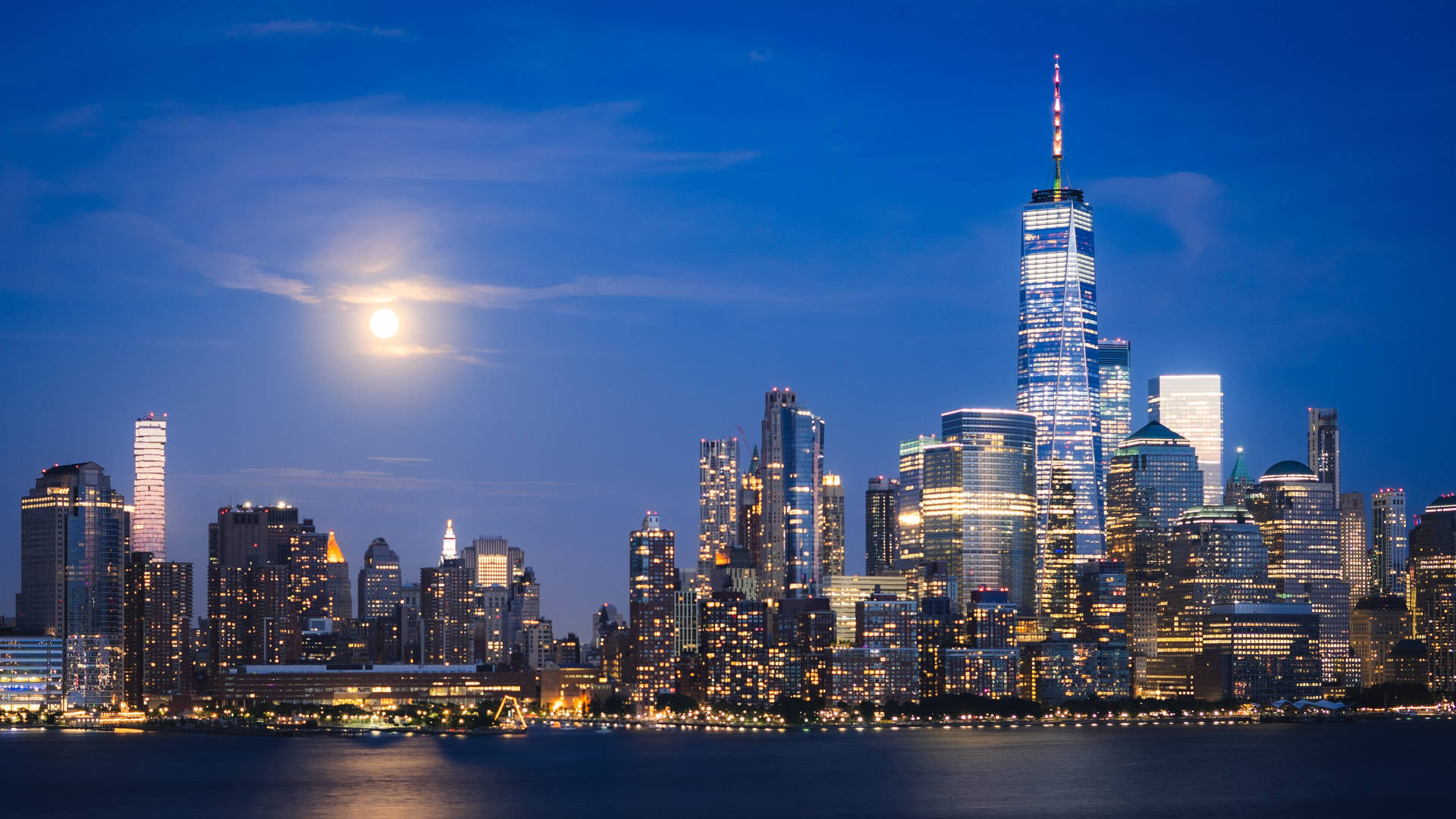 紐約夜景與月亮iPhone壁紙 壁紙 — 紐約令人驚嘆的夜景，明亮的滿月在燈火通明的摩天大樓和反射的水面上閃耀。