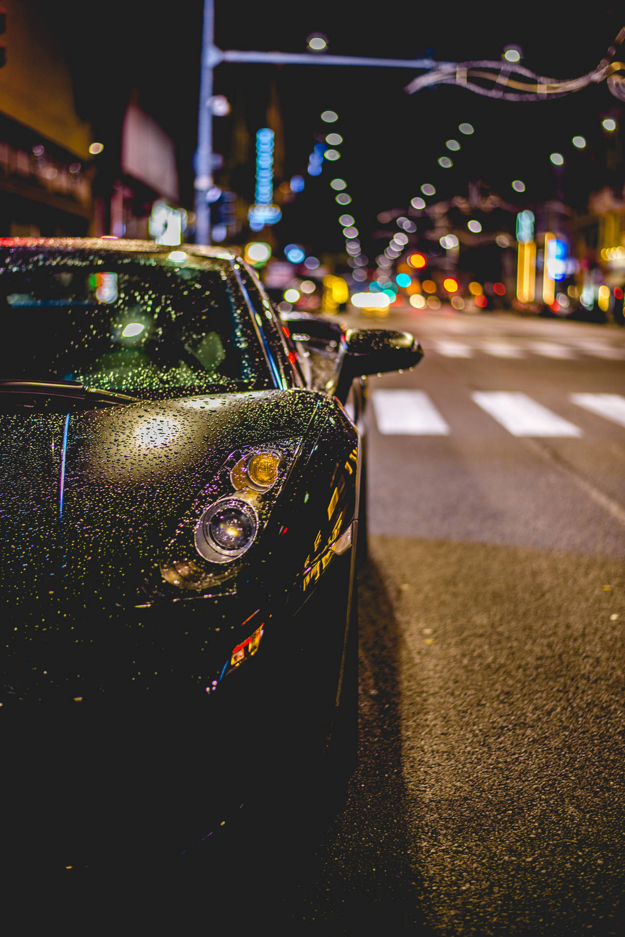 夜間濕漉漉的城市街道上停靠的黑色跑車，帶有模糊的燈光。