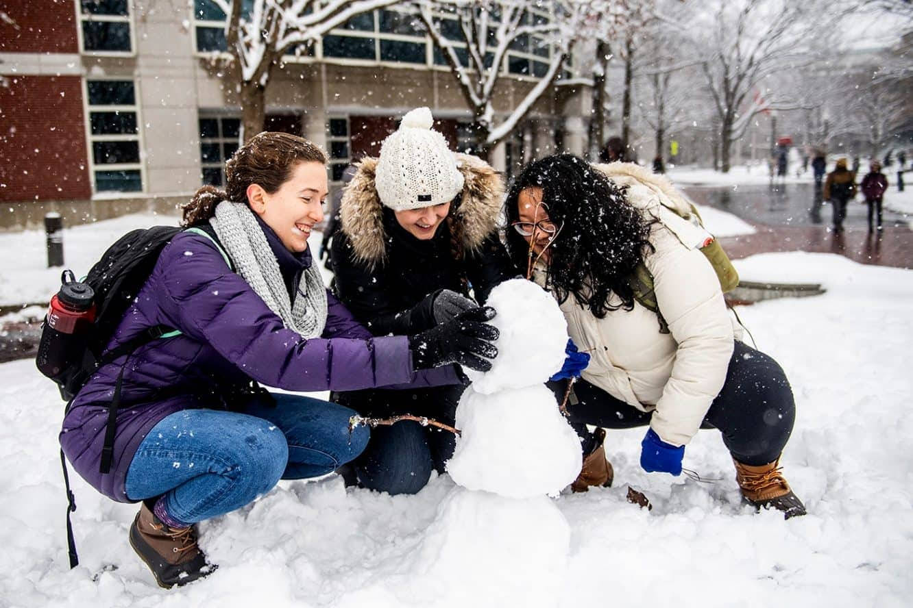 三位微笑的朋友在白雪覆蓋的校園庭院中堆雪人。