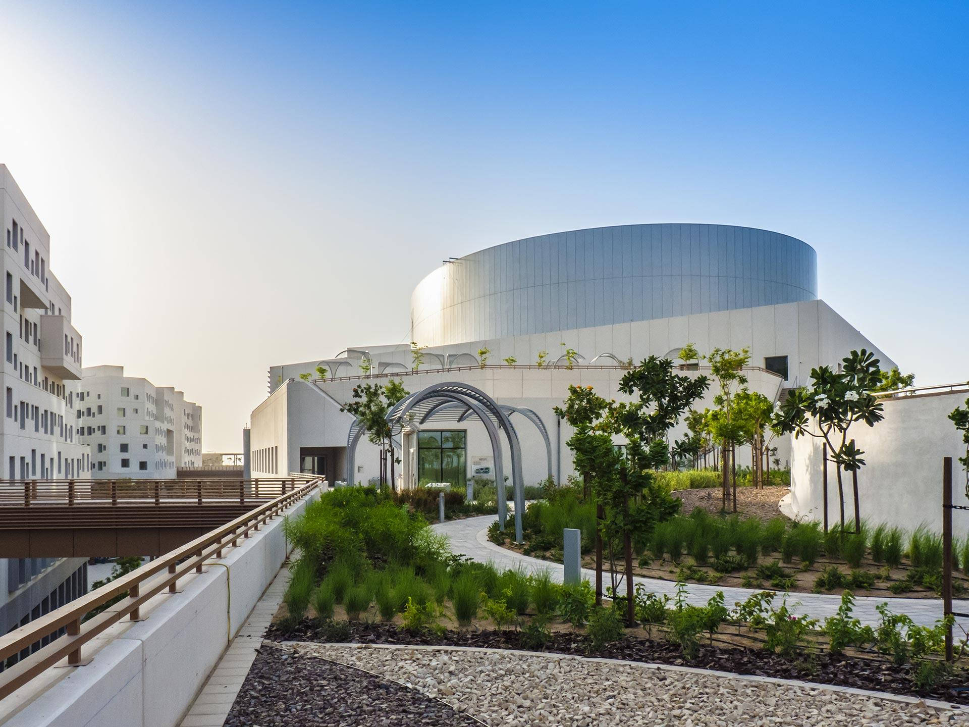 日落時分，現代白色曲線建築，設有屋頂花園和小徑。