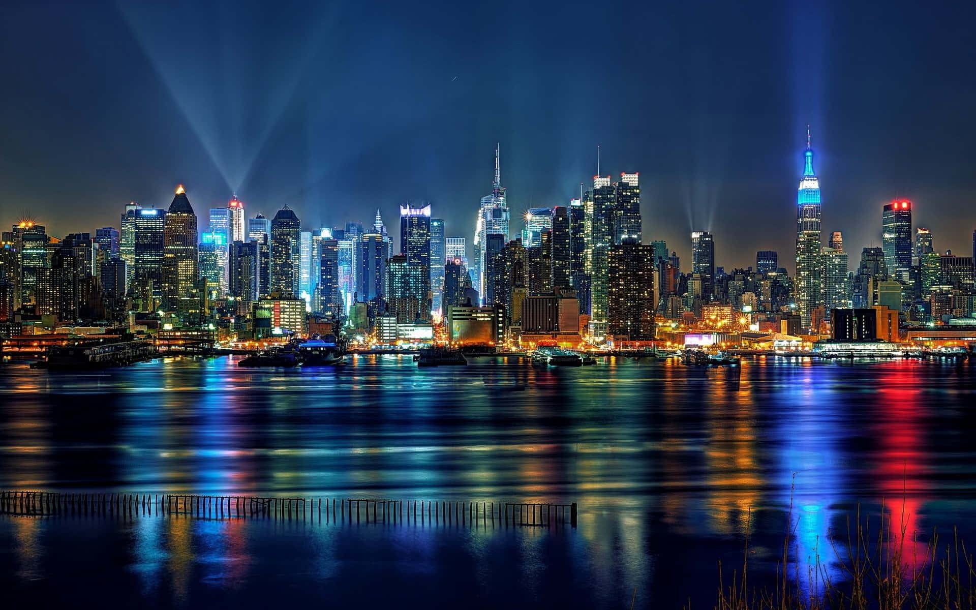 紐約天際線的經典風采 壁紙 — 令人驚嘆的夜景城市景觀，摩天大樓在黑暗的天空中閃耀，它們的燈光倒映在平靜的水面上。