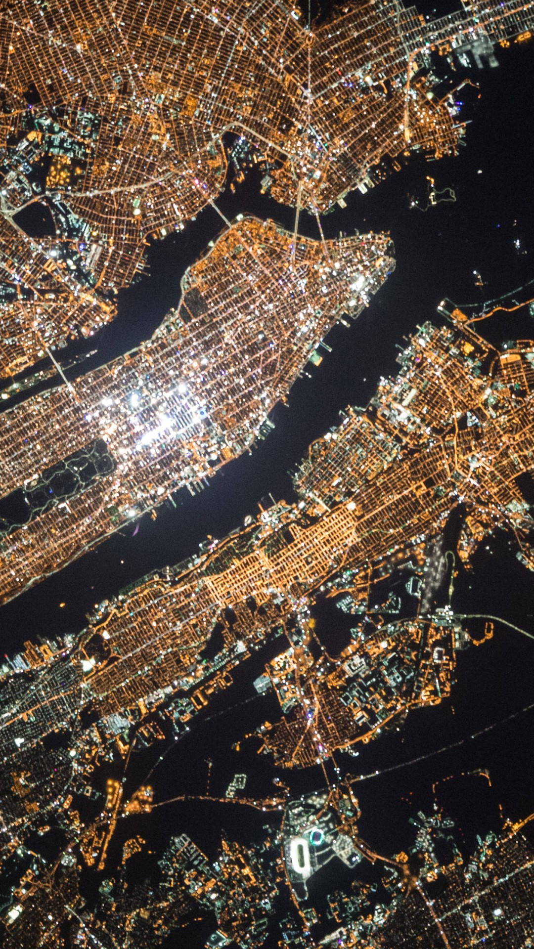紐約市 iPhone X 卫星視圖 壁紙 — 夜晚廣闊城市的鳥瞰圖，金色燈光照亮密集的城市網格和水道。