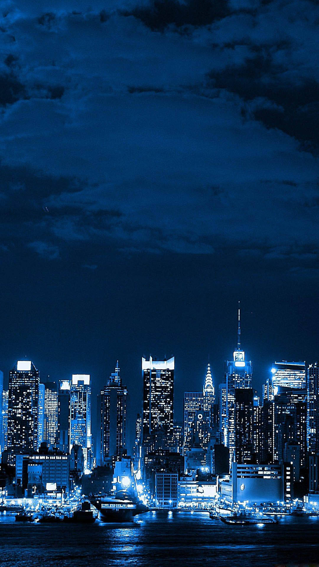 紐約市 iPhone X 海港夜景 壁紙 — 紐約令人驚嘆的夜景，在深藍色多雲的天空下，閃閃發光的摩天大樓倒映在黑暗的水面上。