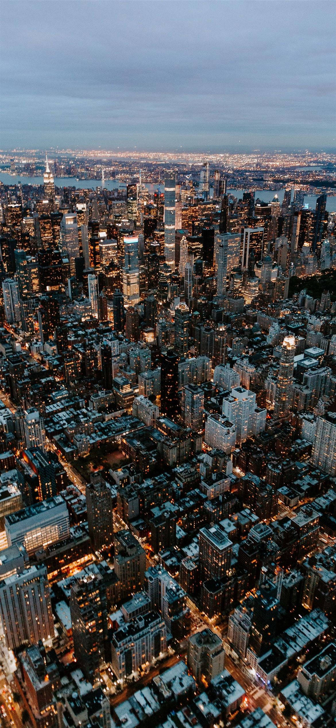 紐約市 iPhone X 空中視角 壁紙 — 黃昏時分密集城市景觀的鳥瞰圖，帶有發光的窗戶和多雲的天空。