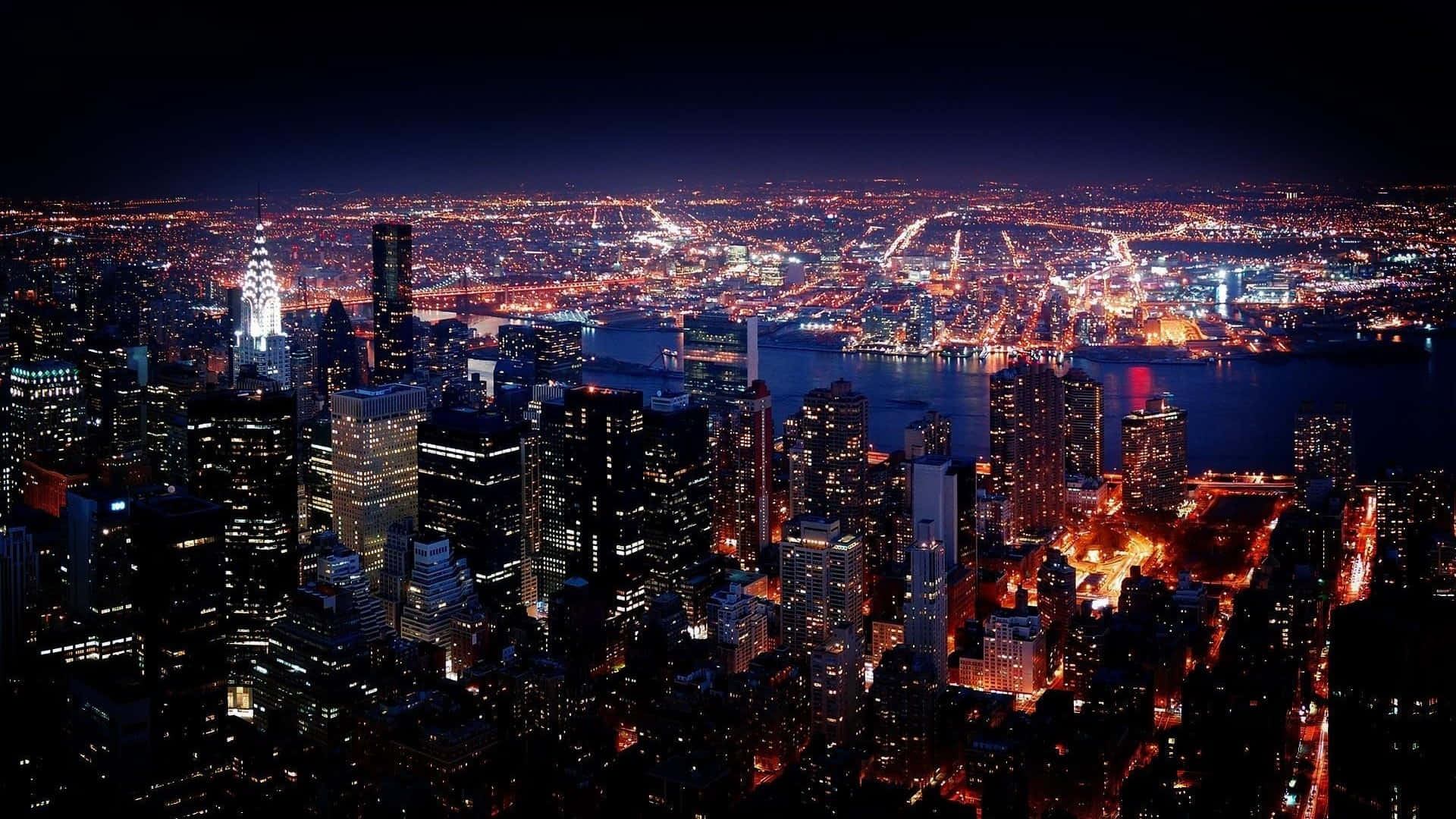 紐約市令人屏息的天際線景觀 壁紙 — 紐約市夜景鳥瞰圖，閃爍的摩天大樓和燈火通明的街道倒映在水面上。