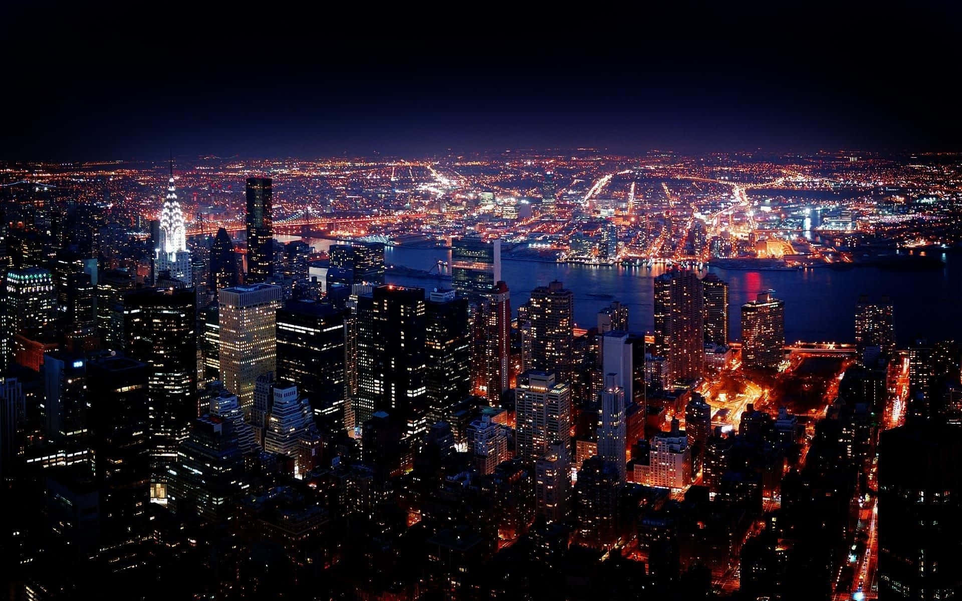 紐約市夜景 壁紙 — 紐約市夜景鳥瞰圖，黑暗水面上有發光的摩天大樓和照明橋樑。