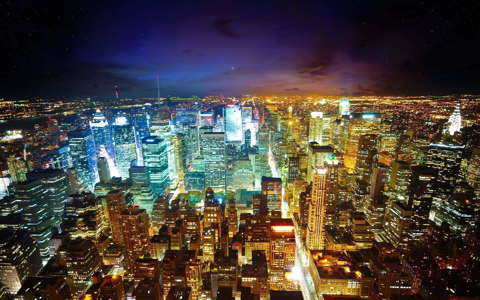 紐約市夜景 壁紙 — 深紫色天空下，閃爍的摩天大樓和鮮豔霓虹燈構成的廣闊城市夜景鳥瞰圖。