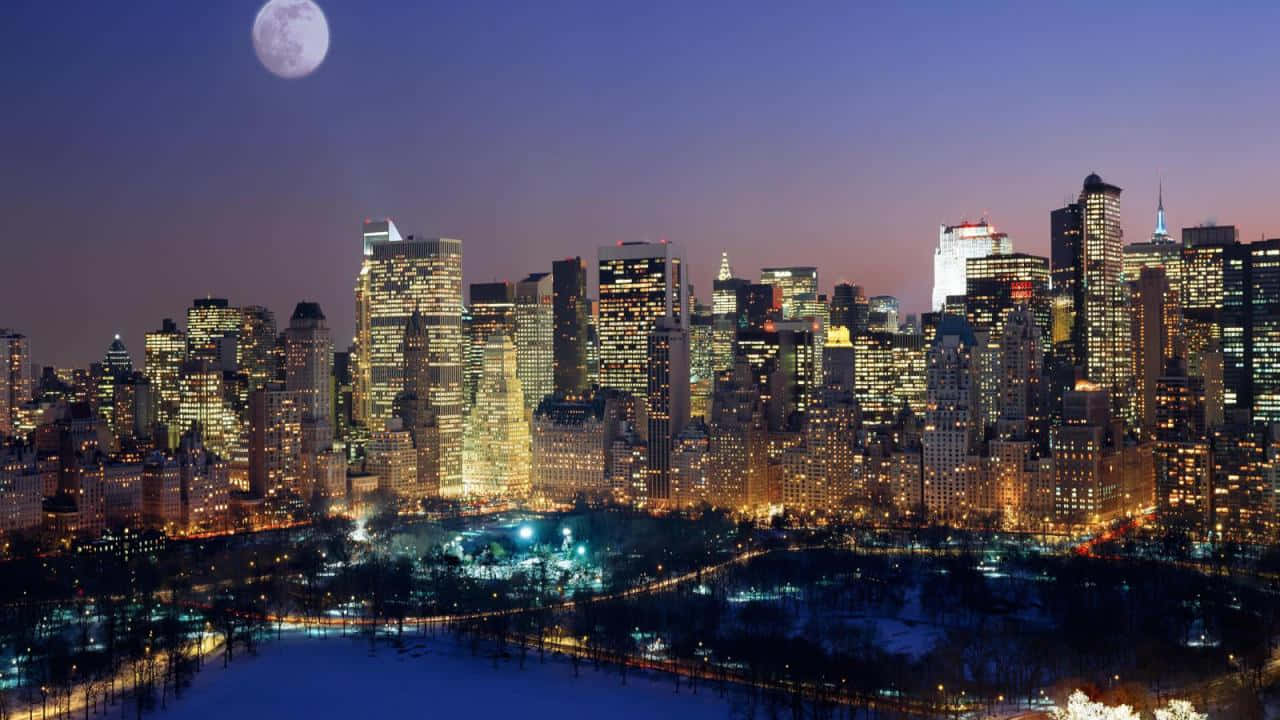 紐約市夜景的壯麗視角 壁紙 — 黃昏時分，白雪覆蓋的城市天際線，一輪滿月在燈火通明的摩天大樓和中央公園上方閃耀。