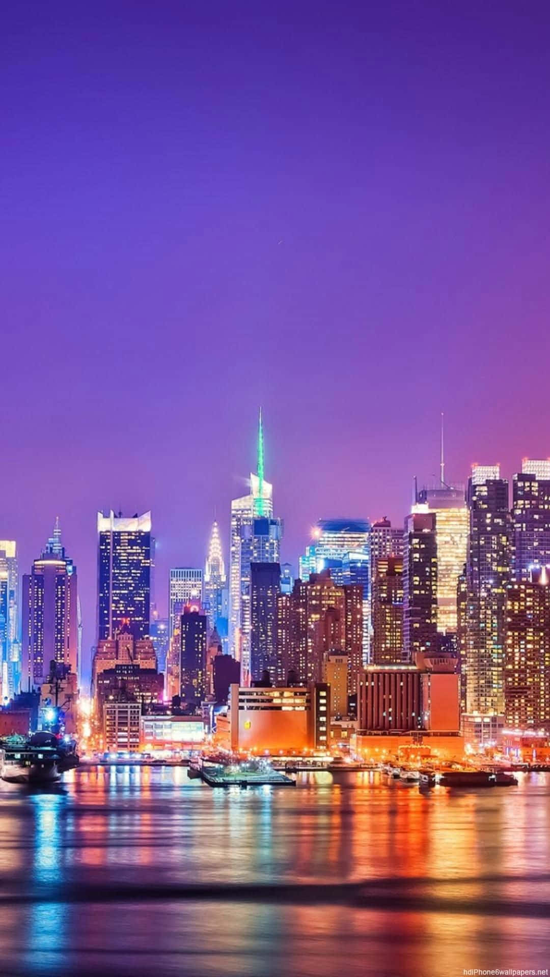 紐約市夜景絢麗色彩 iPhone 壁紙 — 黃昏時分充滿活力的城市天際線，閃爍的摩天大樓倒映在下方平靜的水面上。