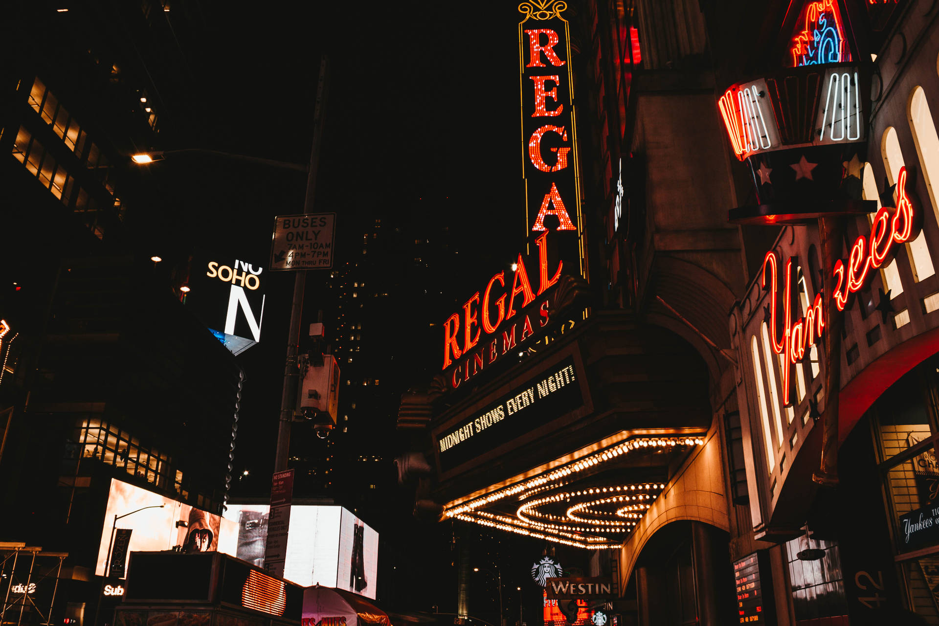 夜晚霓虹燈照亮的城市街道，帶有 Regal Cinemas 和 Yankees 標誌。