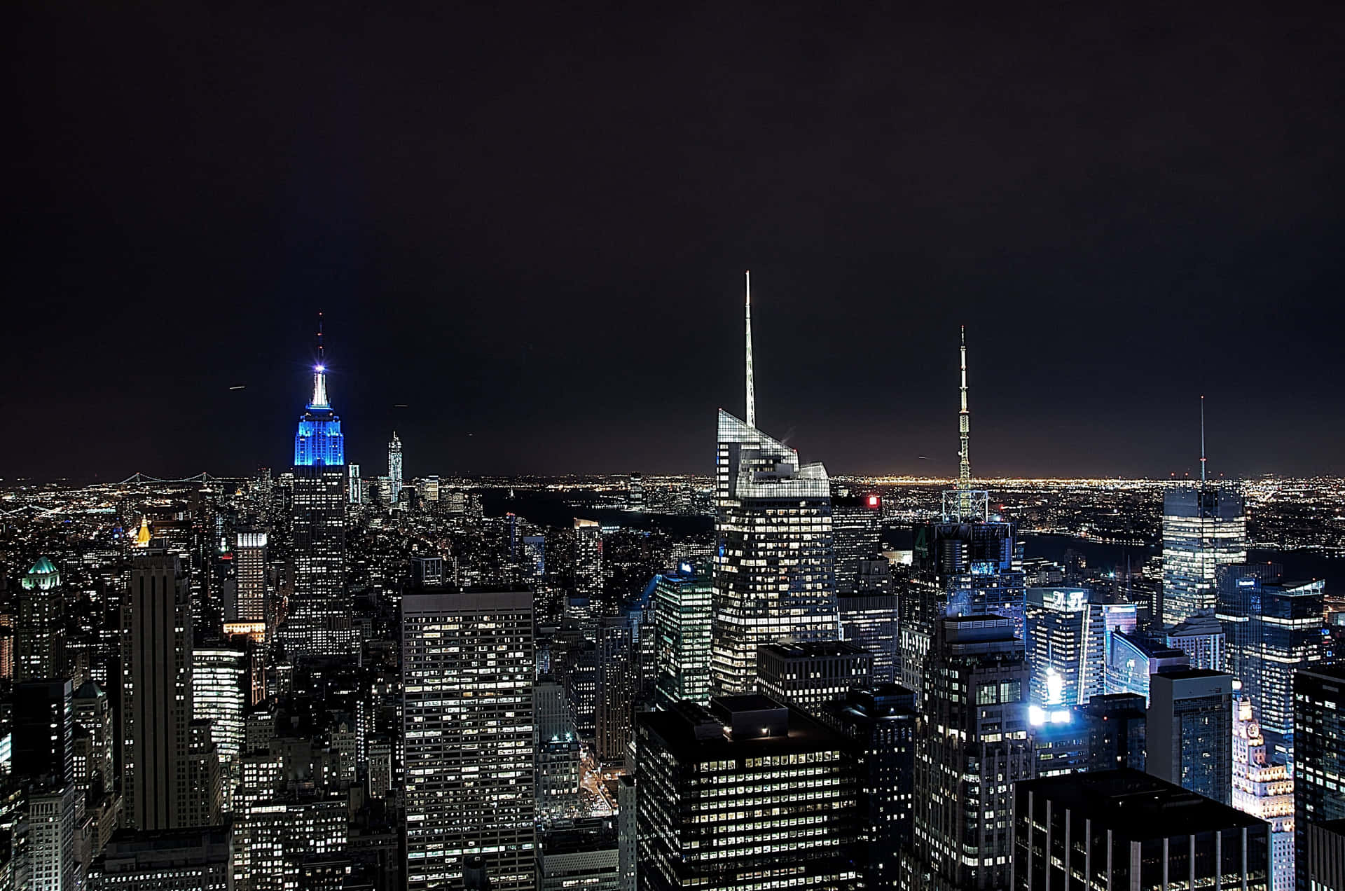 紐約市天際線的夜景，摩天大樓燈火通明，帝國大廈發出藍色光芒。