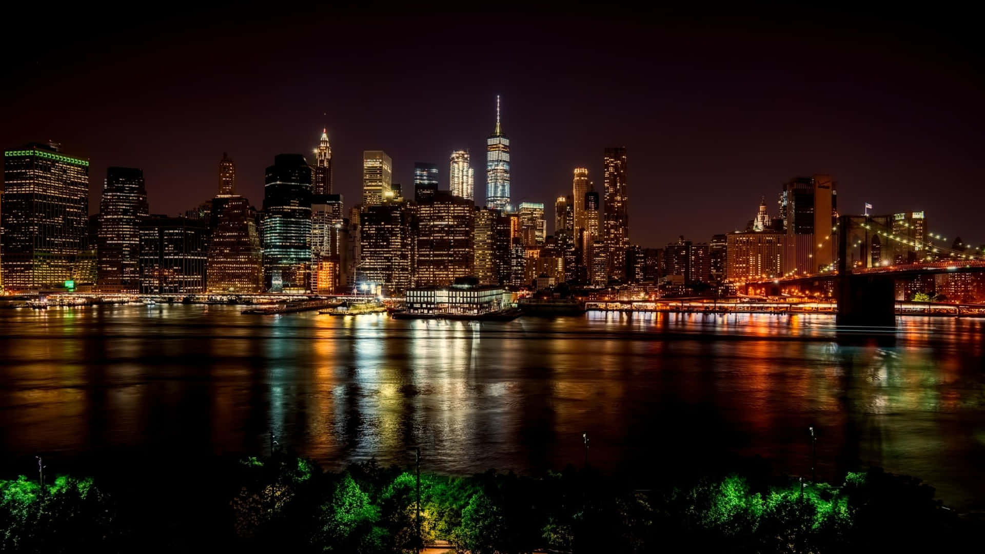 紐約天際線的夜景，有發光的建築物和水面上的橋樑。