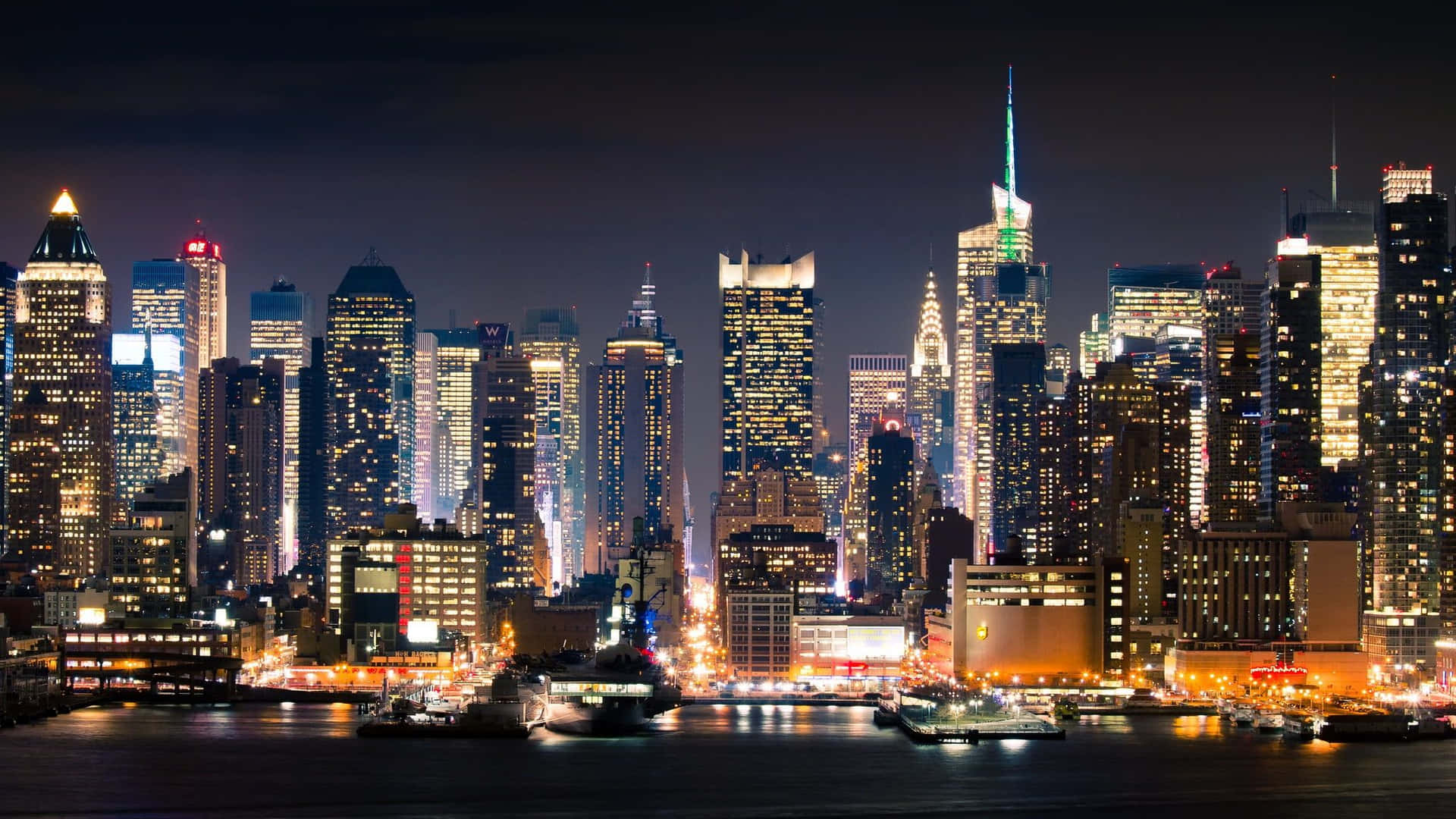 紐約市天際線的夜景，建築物閃閃發光，水面倒影清晰。