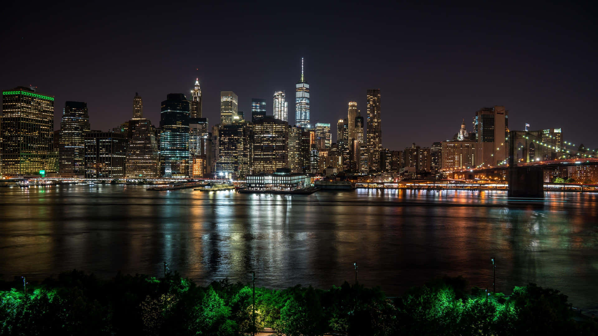 紐約天際線的夜景，燈火通明的建築物和水上的橋樑。