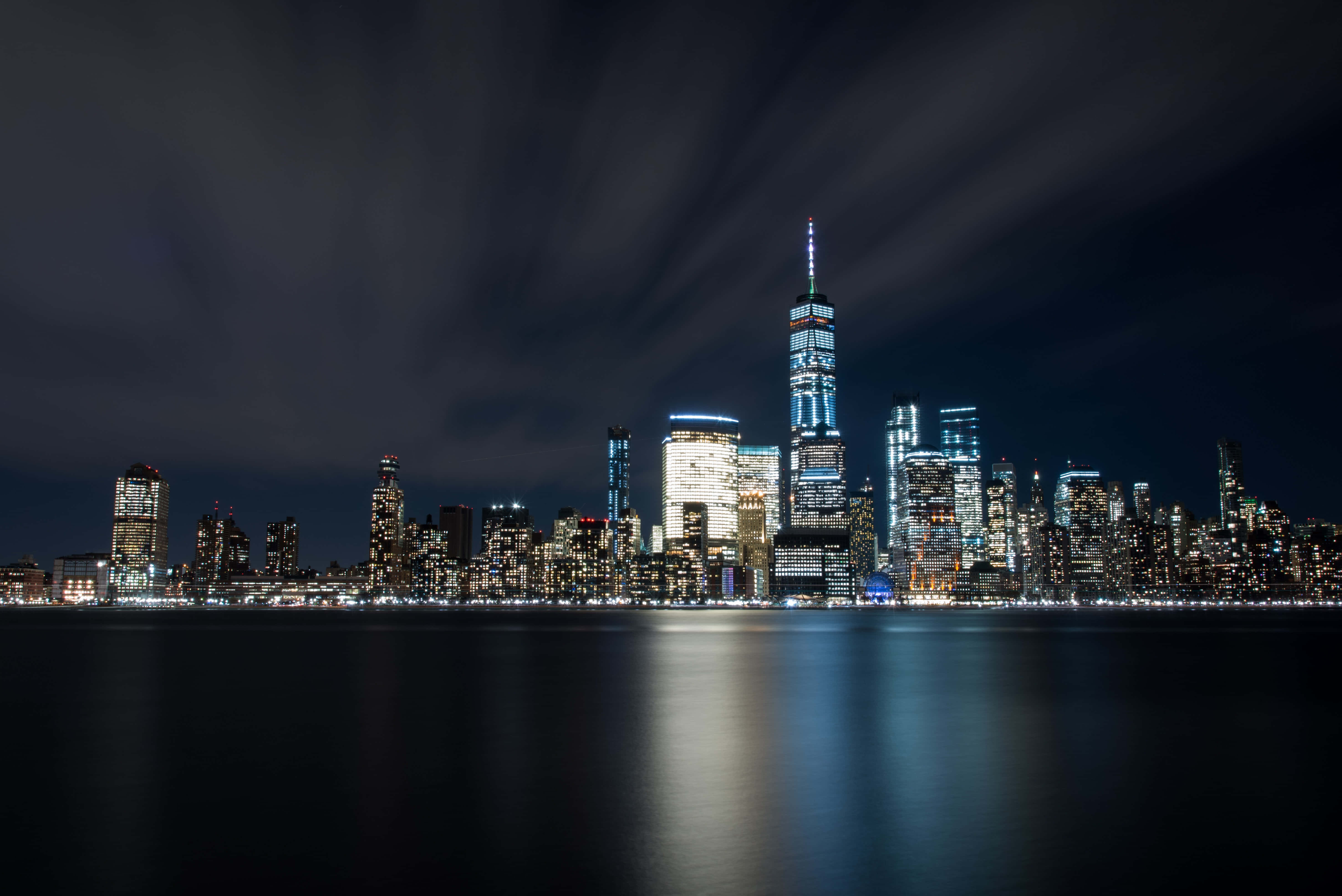 紐約市 桌布 壁紙 — 紐約市天際線的壯麗夜景，摩天大樓在黑暗的天空下照亮，倒映在平靜的水面上。