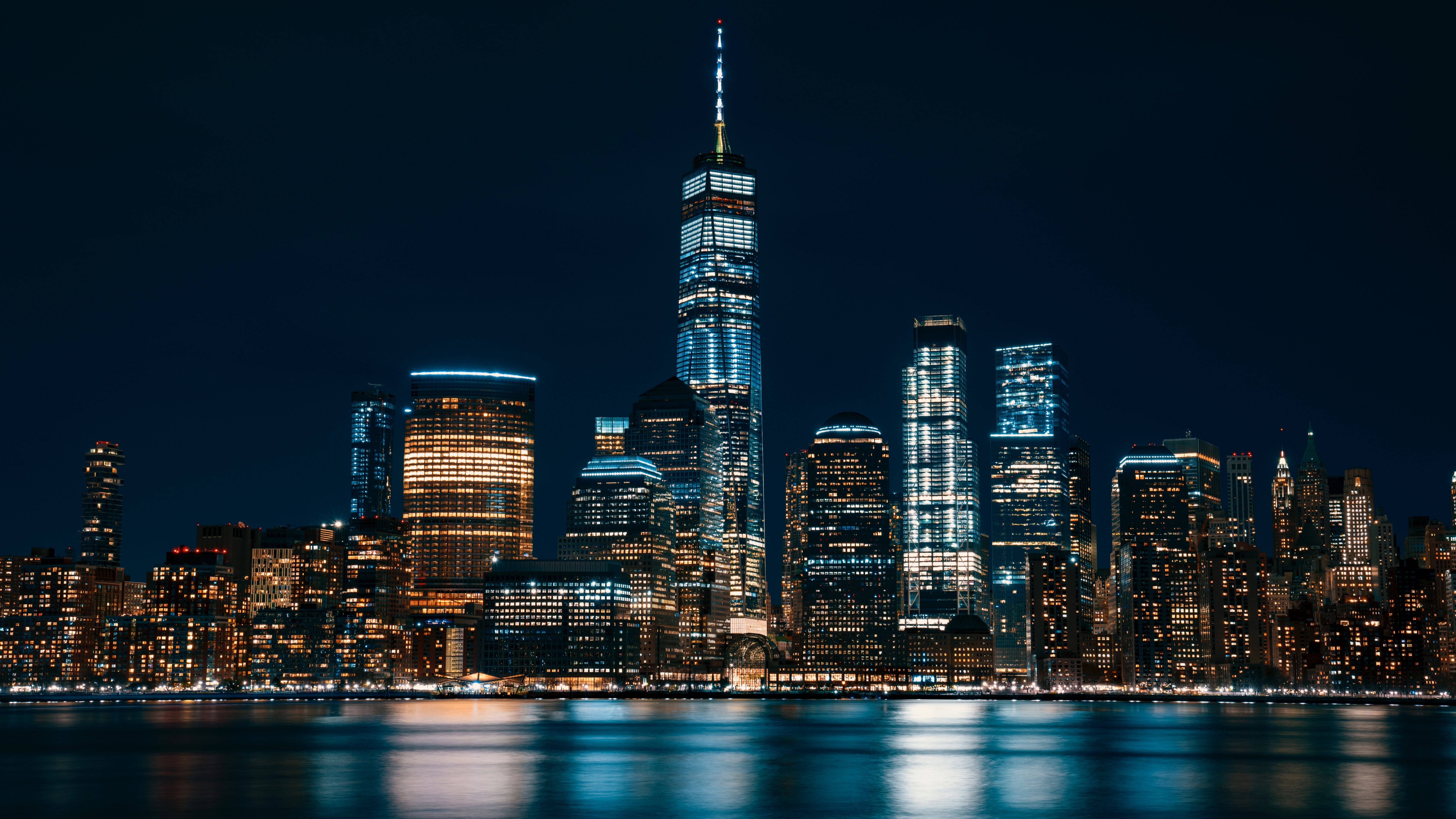 Skyscraper 桌布 壁紙 — 紐約市天際線的壯麗夜景，燈火通明的摩天大樓倒映在下方平靜的水面上。