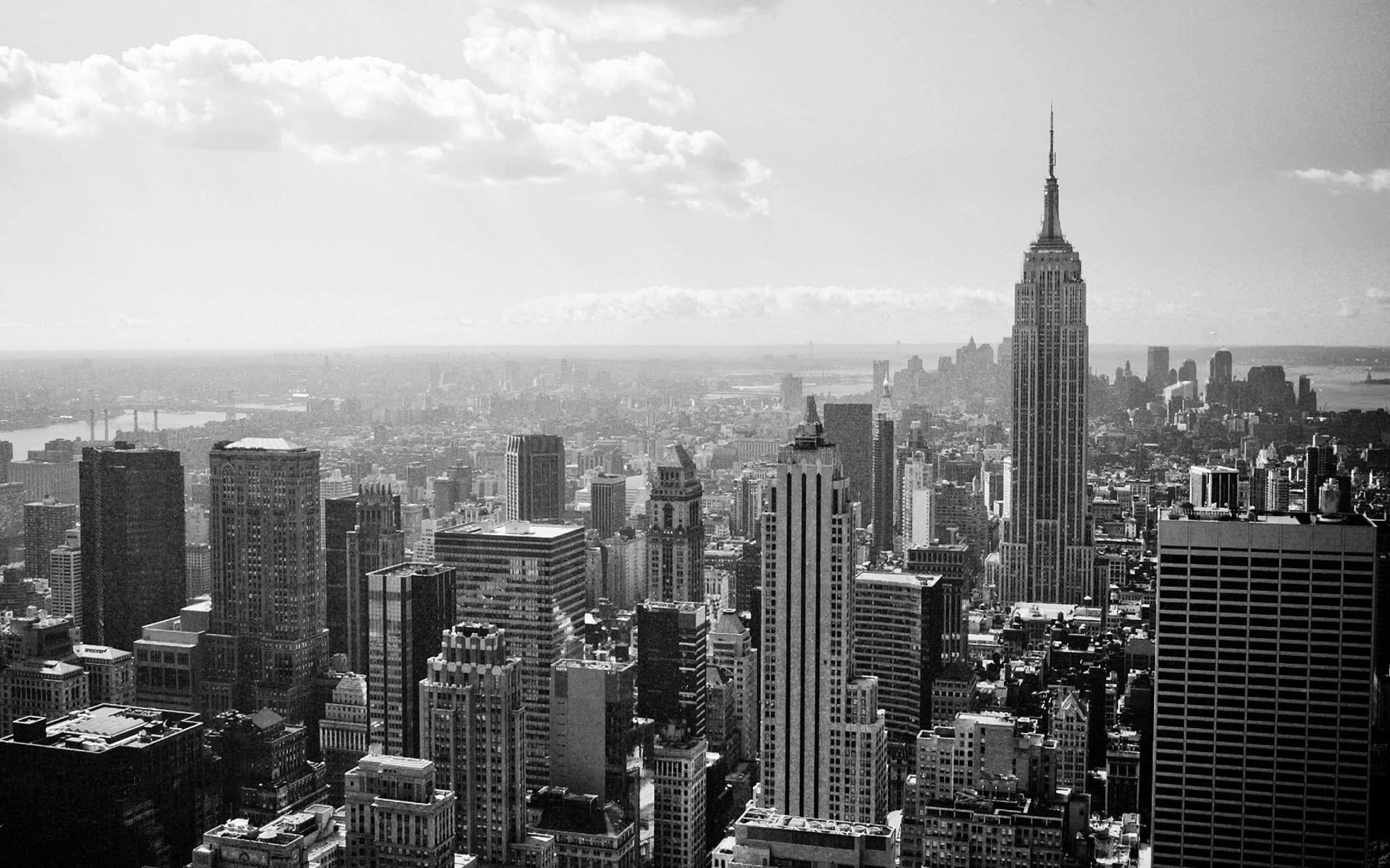 New York City 桌布 壁紙 — 紐約市天際線的黑白全景視圖，以雲層天空下的帝國大廈為主導。