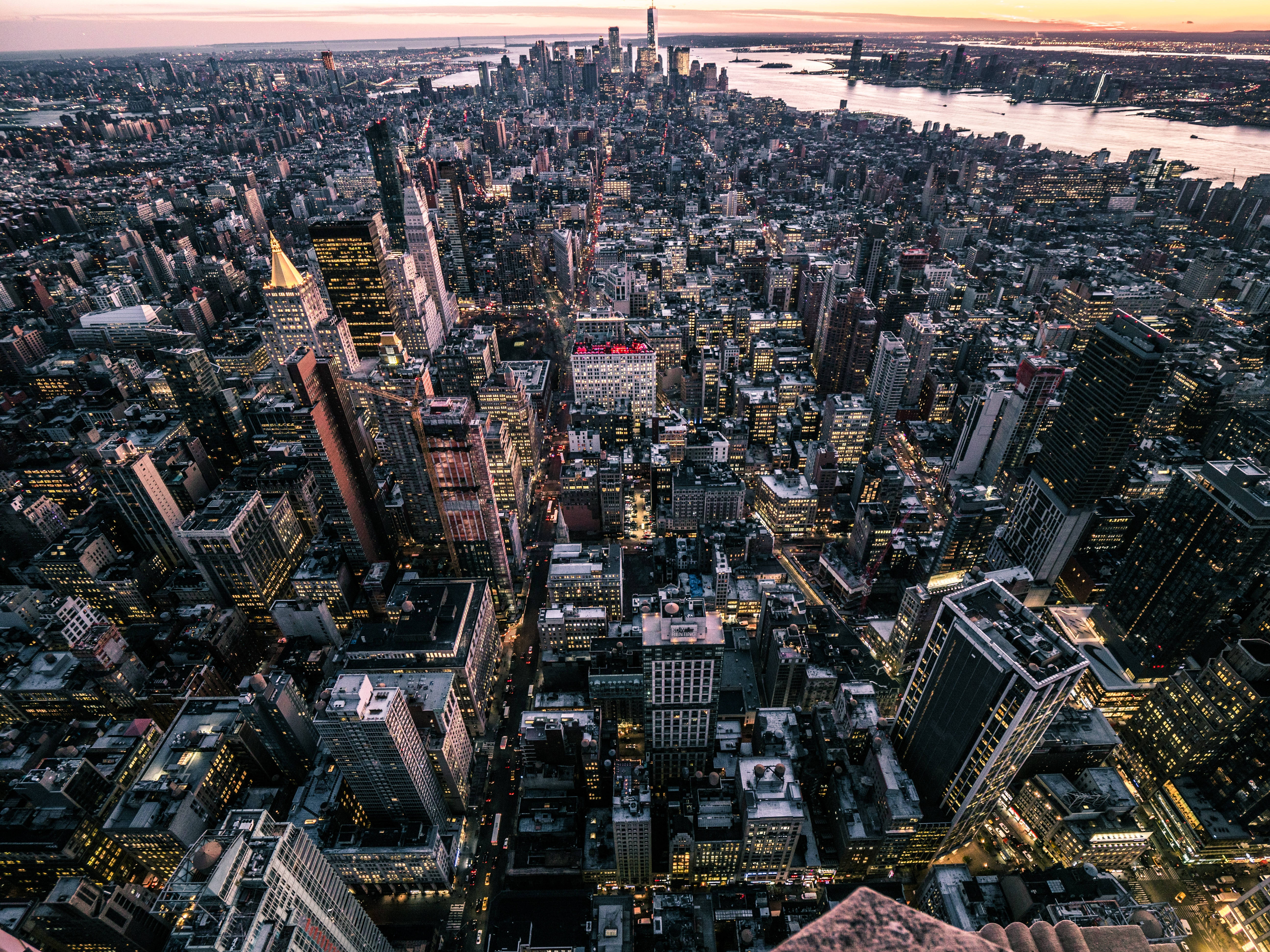 紐約市景俯瞰圖 壁紙 — 黃昏時分紐約市的鳥瞰圖，閃爍的摩天大樓和河流映照著逐漸褪色的橙色天空。