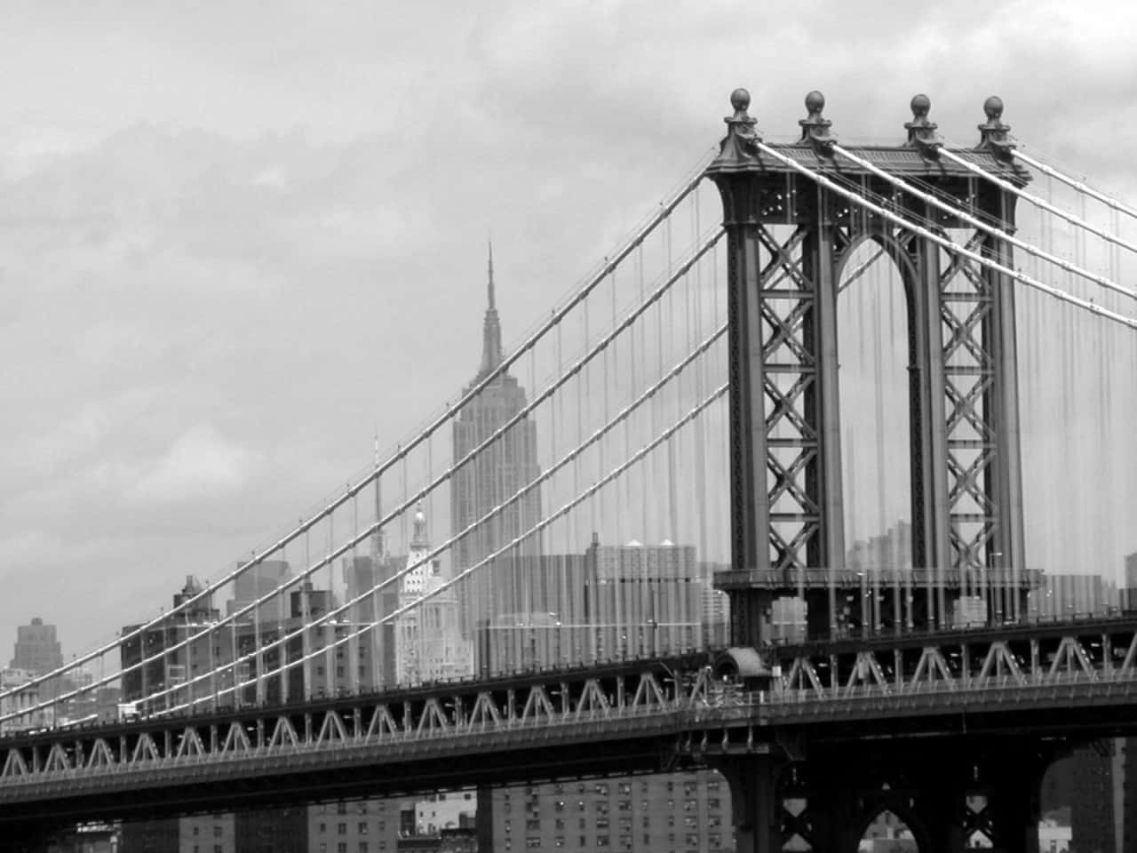 紐約市標誌性的天際線 壁紙 — 曼哈頓大橋的單色景觀，帝國大廈在其鋼結構後方升起，天空多雲。