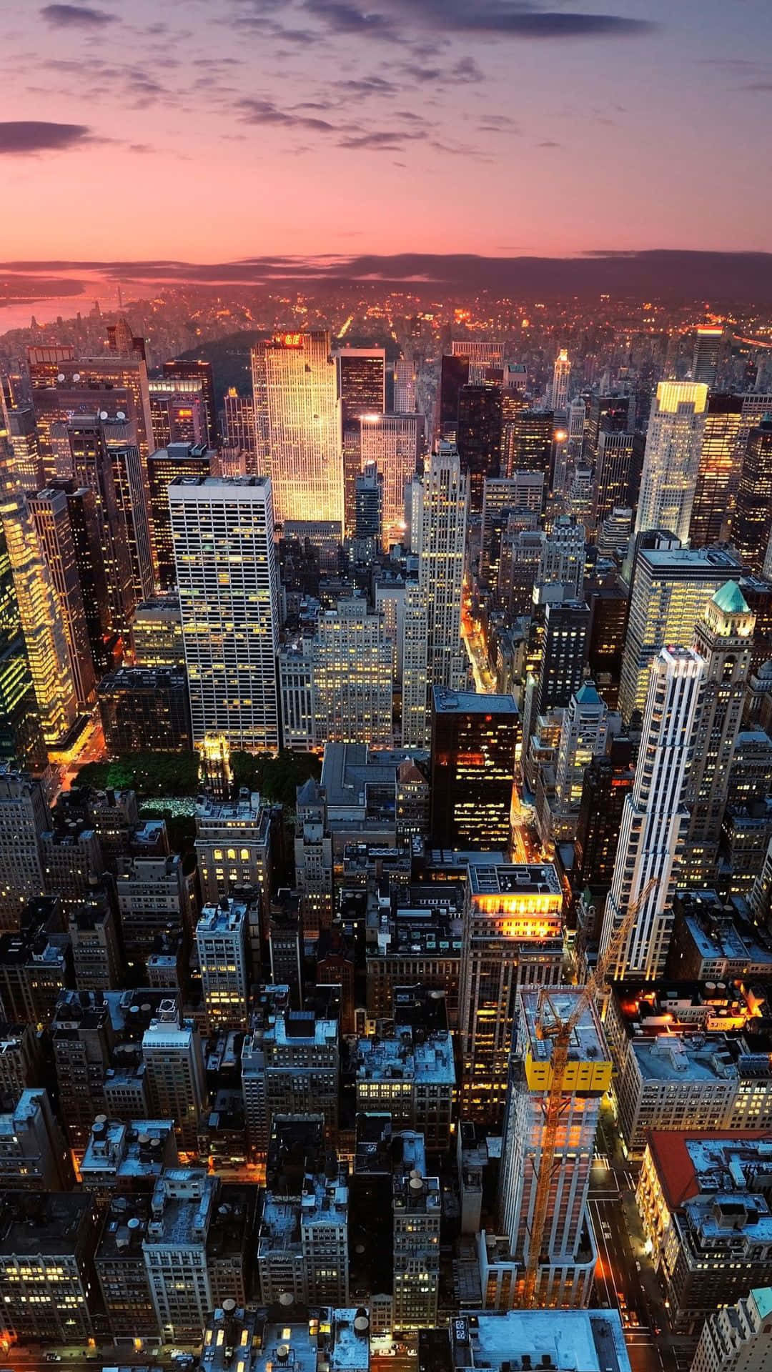 紐約市的繁華與 Android 的便利完美結合 壁紙 — 黃昏時分密集城市景觀的鳥瞰圖，摩天大樓在粉紅色和紫色的天空下閃閃發光。