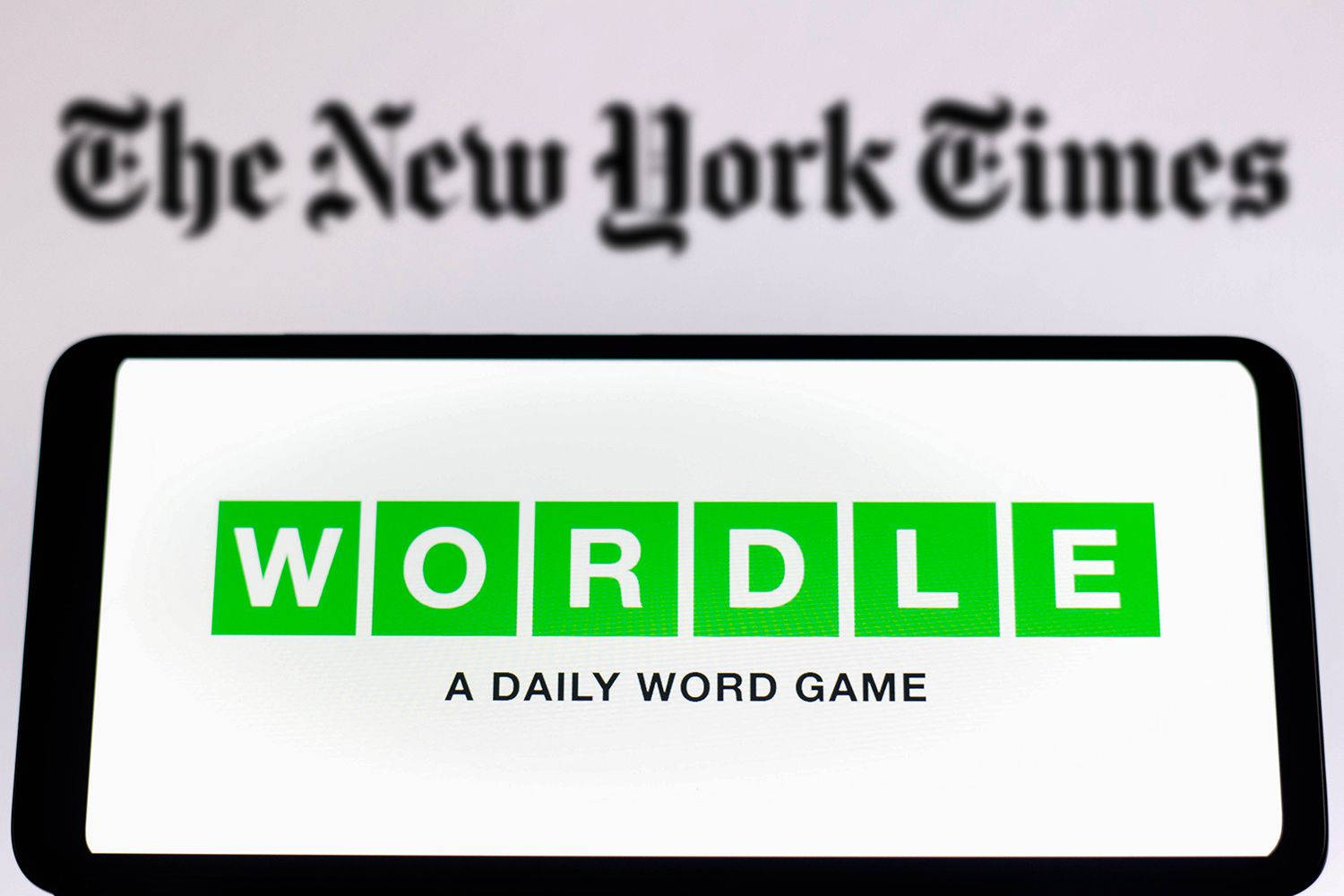 智能手機顯示Wordle遊戲標誌，背景係模糊嘅《紐約時報》。