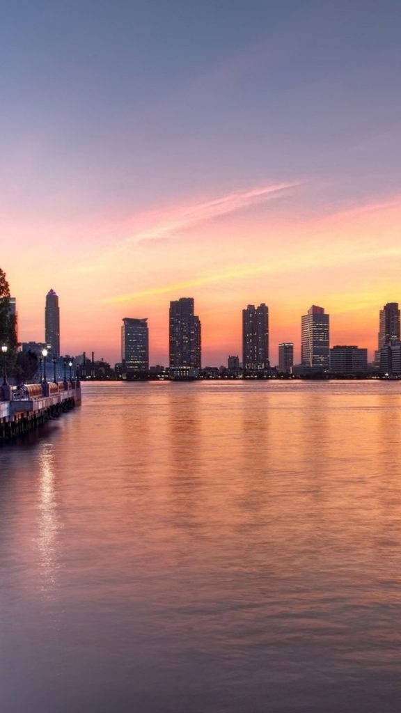 日落時分的城市天際線，建築物倒映在平靜的水面上