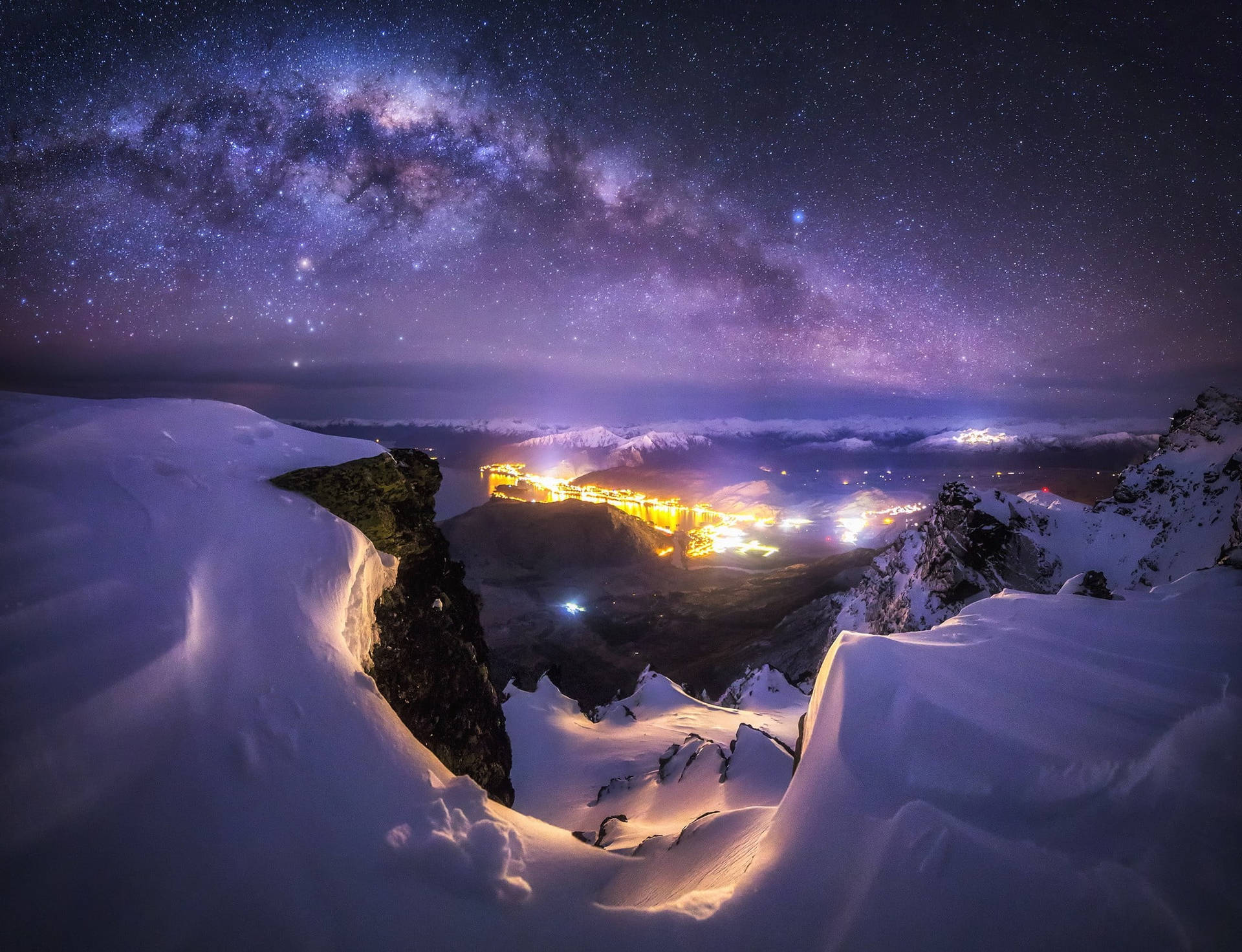 白雪覆蓋的山俯瞰著一個在星空和銀河下的明亮山谷。