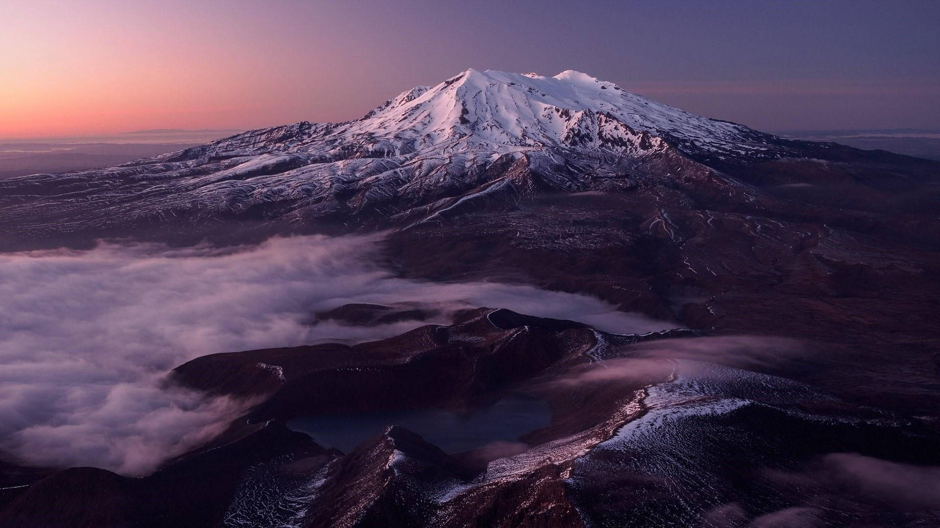 紐西蘭魯阿佩胡山壯麗景色 壁紙 — 白雪覆蓋的山峰在黎明時分從雲海中升起，天空呈現粉紅色和紫色。
