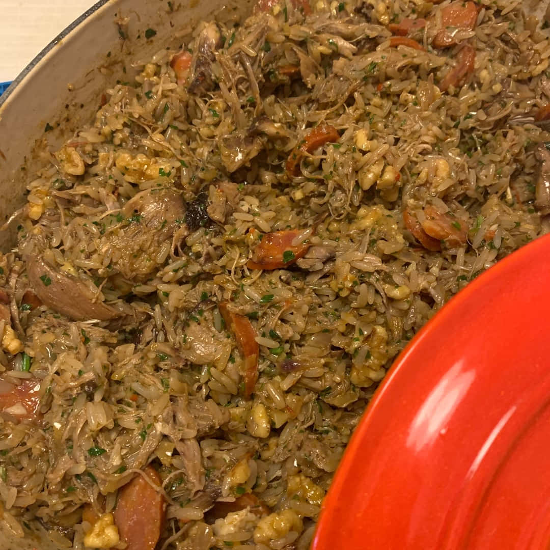 純樸鴨飯近距離特寫 壁紙 — 陶瓷鍋中嘅鹹味米飯菜餚，配以雞肉腸絲同香草，旁邊有個紅色碟嘅特寫。
