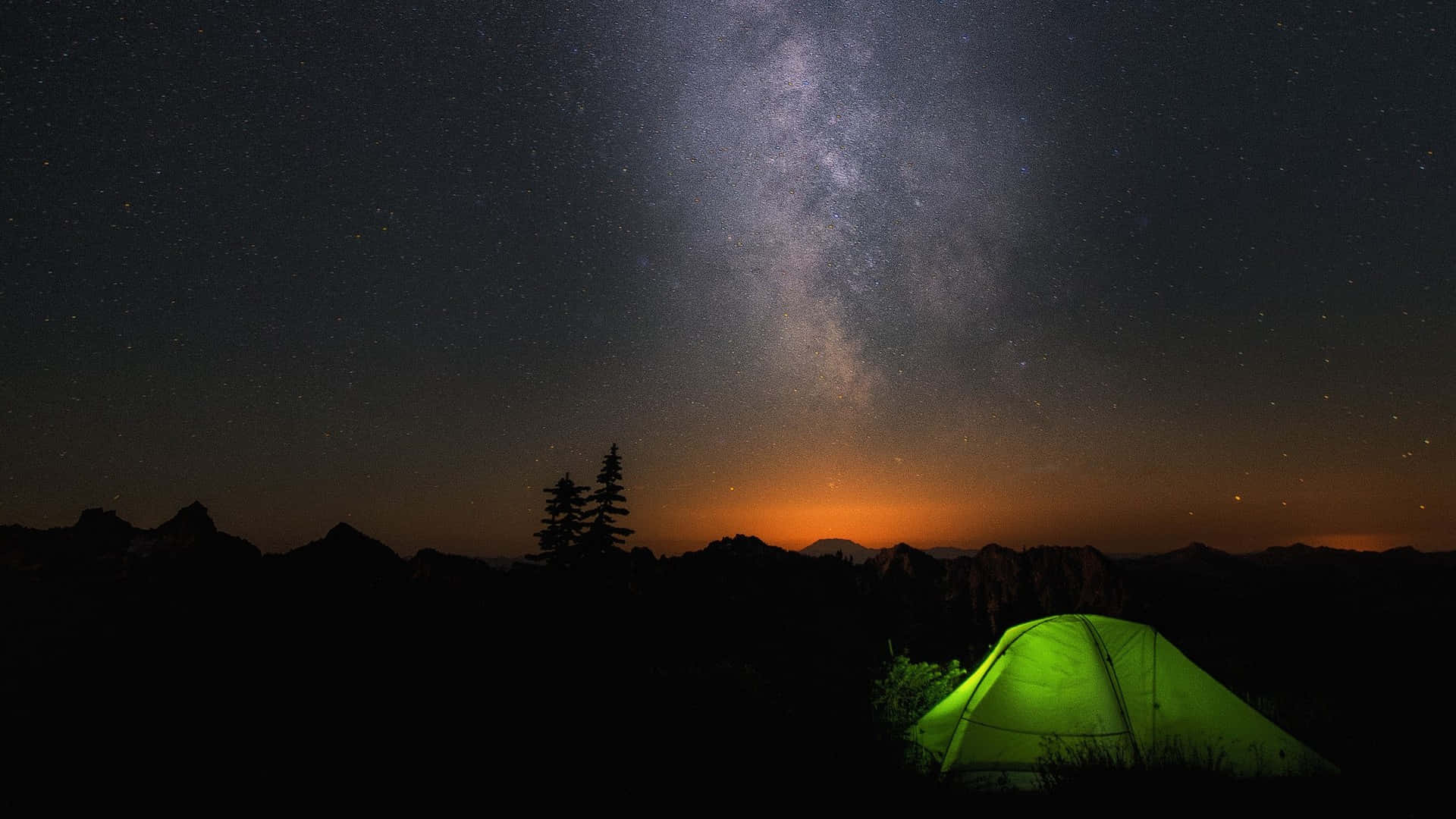純淨呈現的 Windows 預設背景 壁紙 — 在黑暗山脈中，一頂發光的綠色帳篷，上方是壯麗的星空，銀河拱跨天際。