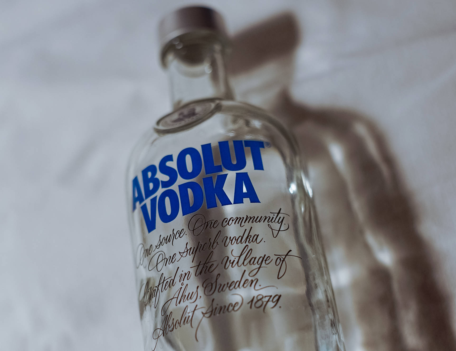 白色布料上一個帶有藍色文字的透明Absolut Vodka酒瓶。