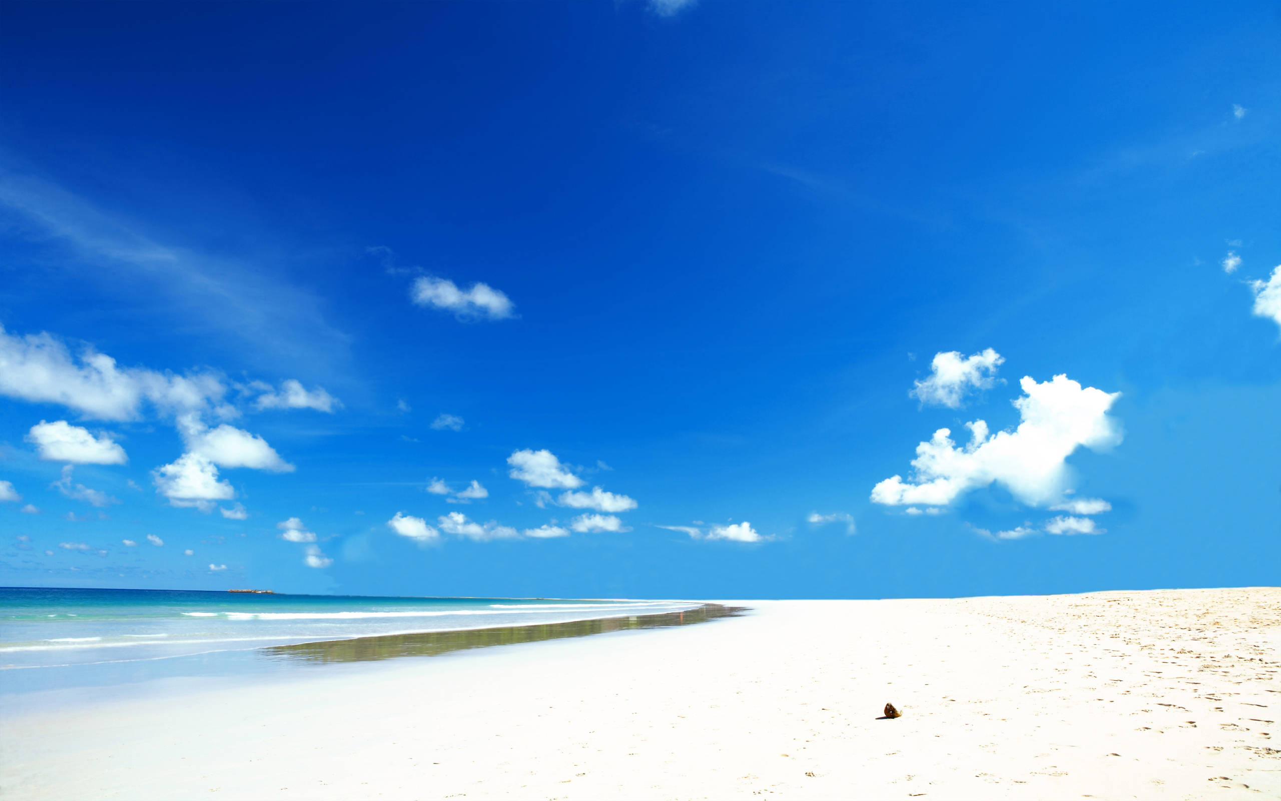 Beach Desktop 桌布 壁紙 — 純淨的白色沙灘在點綴著蓬鬆白雲的鮮豔藍天下延伸。