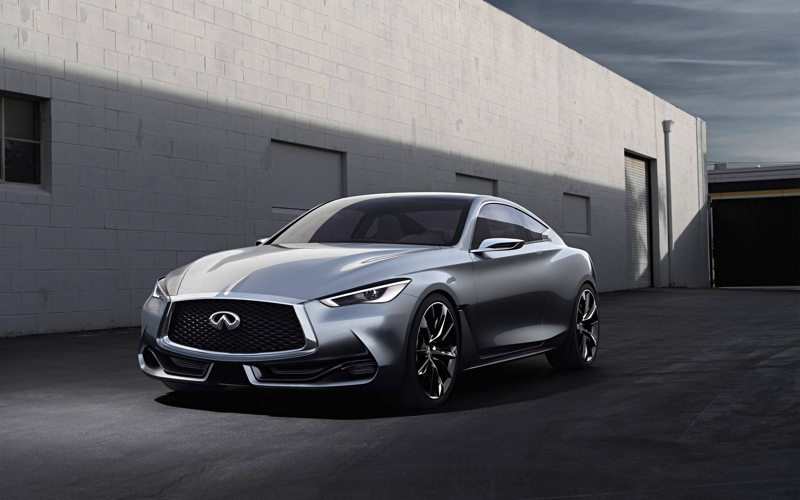 純淨銀色2018款英菲尼迪Q60 壁紙 — 一輛時尚的銀色 Infiniti 跑車停放在 stark 白色磚砌倉庫前，在戲劇性的燈光下。