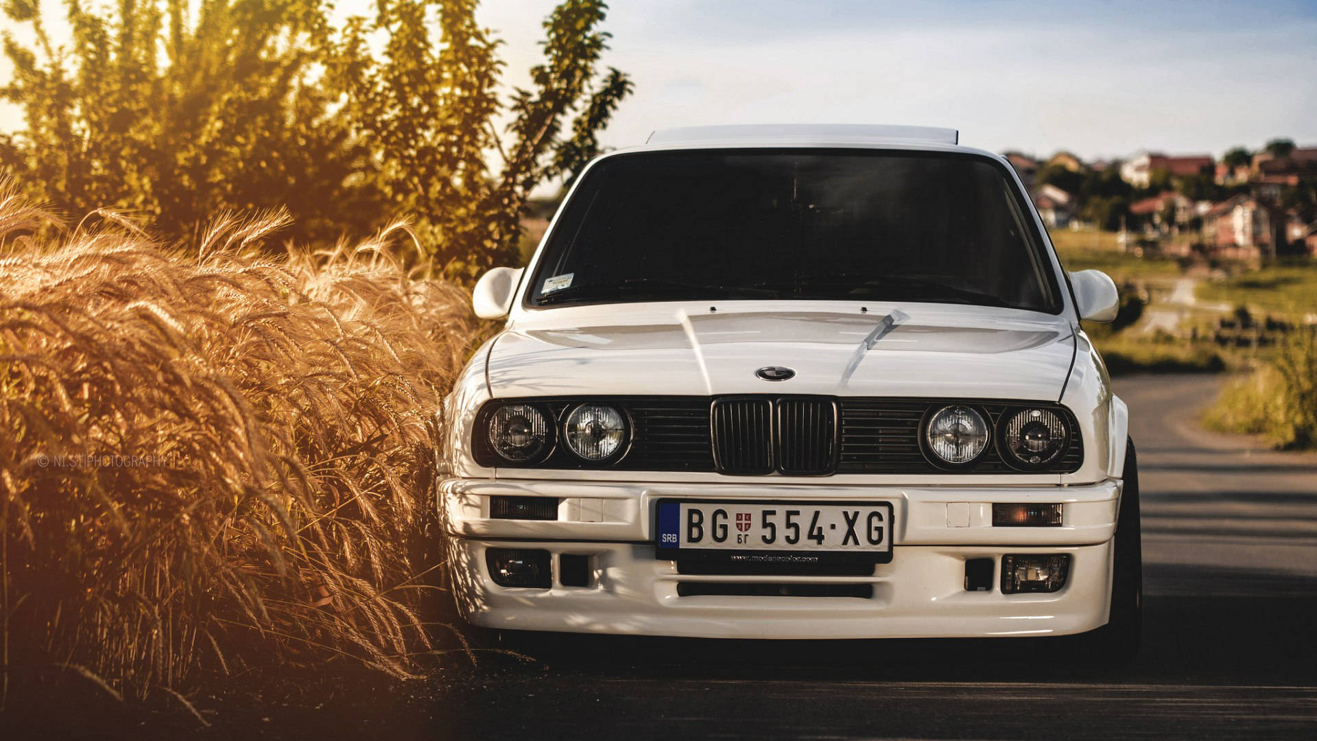 白色經典BMW E30停在日落時分的金色麥田旁。