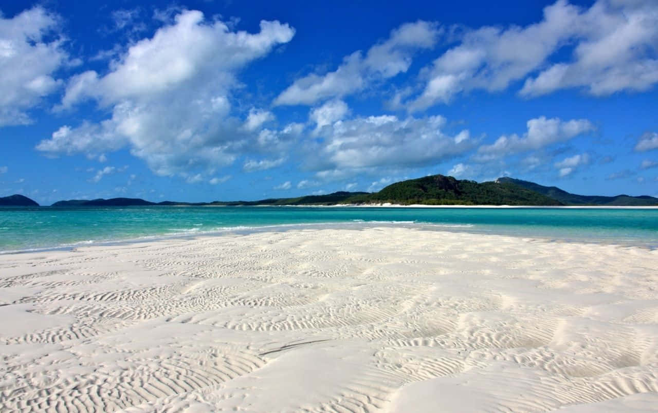 Australia Beach 桌布 壁紙 — 純白沙灘，碧綠海水，遠方翠綠山丘，藍天白雲。