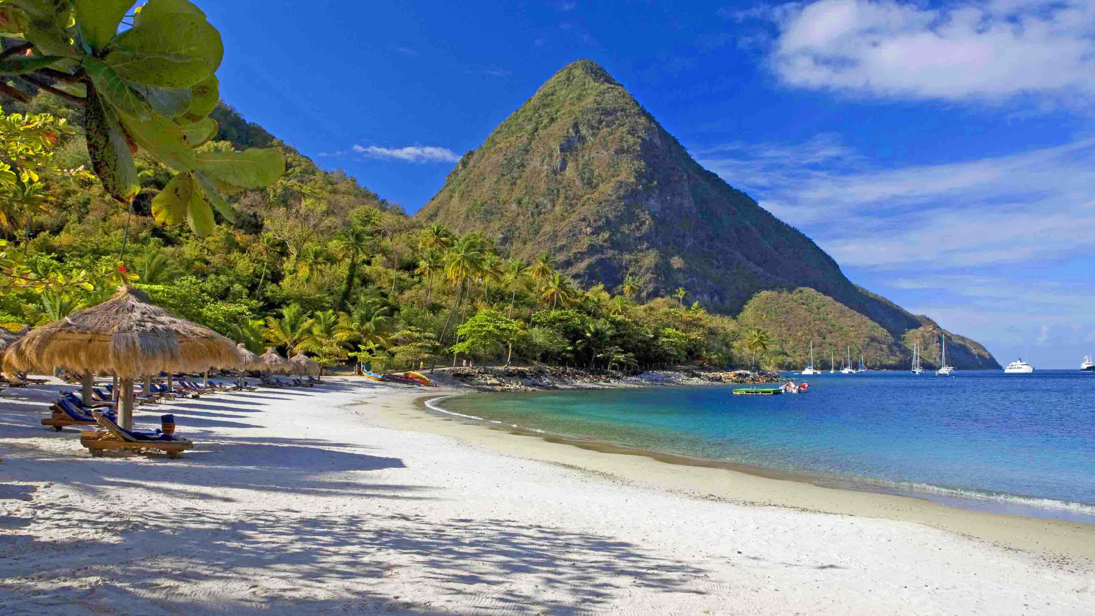 Beach Resort 桌布 壁紙 — 純白沙灘環繞著碧綠海水，棕櫚樹後方，在明亮的藍天下，一座鬱鬱蔥蔥的青山聳立。