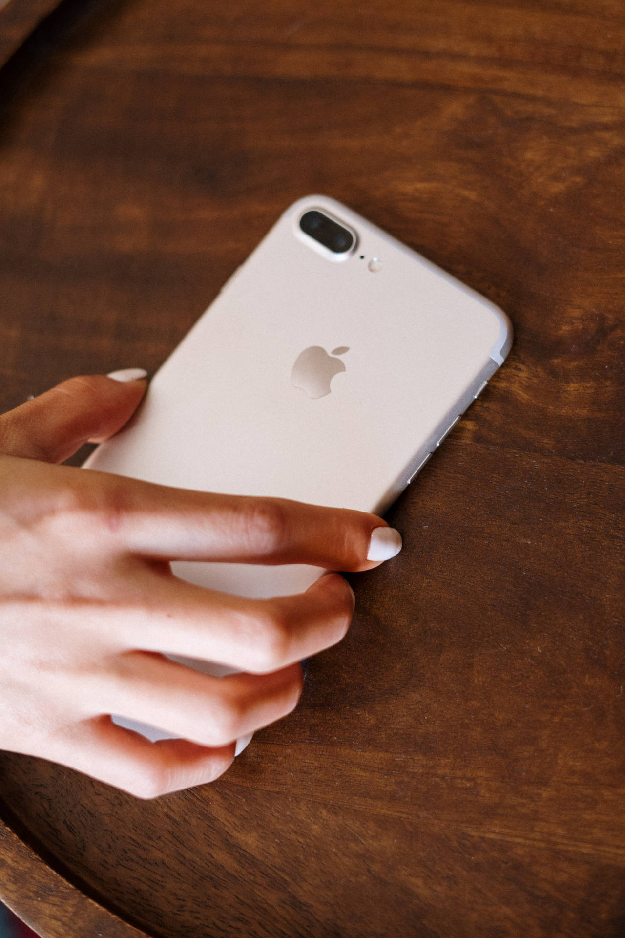 一隻手在木質表面上拿著一部銀色iPhone。