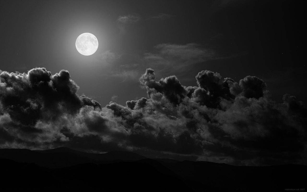 純黑底配月與雲 壁紙 — 一輪明亮的滿月穿過戲劇性的雲層，照耀在剪影般的山脈上，呈現出鮮明的黑白夜景。