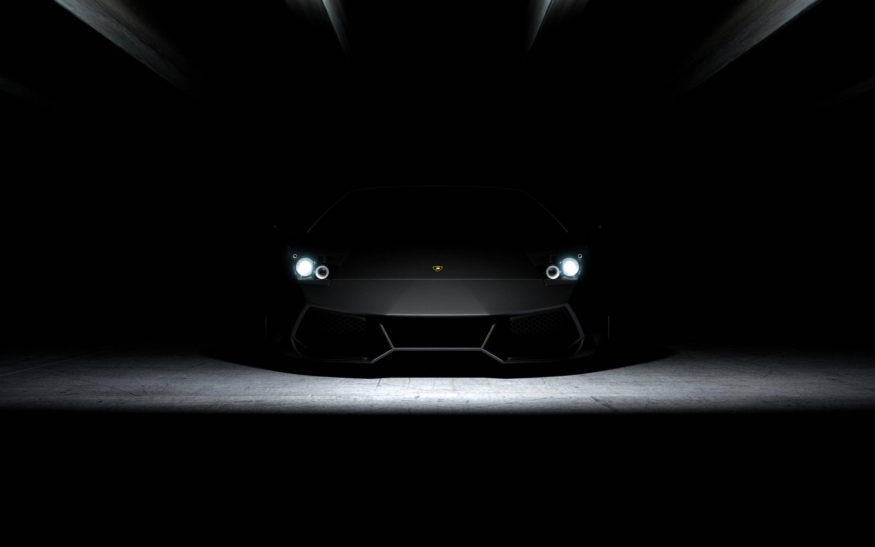 純黑蘭博基尼跑車 壁紙 — 一輛時尚的黑色林寶堅尼 Aventador 在黑暗的攝影棚中被聚光燈照亮，投射出戲劇性的陰影。