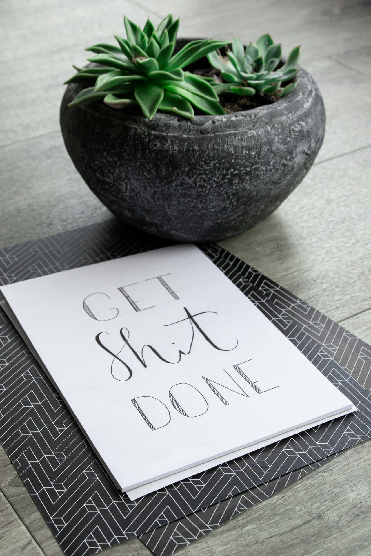 紙上寫著「Get Shit Done」 壁紙 — 一張勵志語錄卡放在幾何圖案墊上，旁邊是一個有紋理的石盆，裡面種著充滿活力的綠色多肉植物。