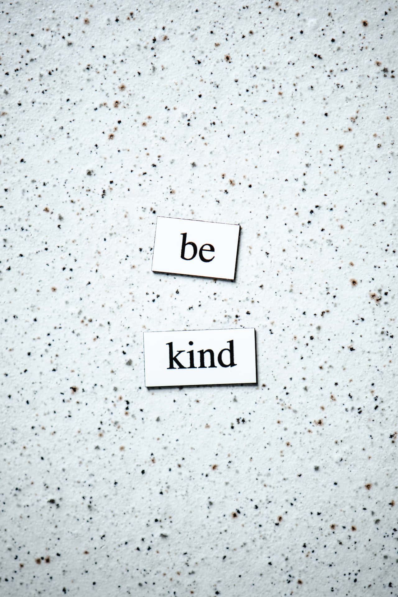 兩張卡片上寫著「be kind」，放在斑駁的灰色牆壁上。