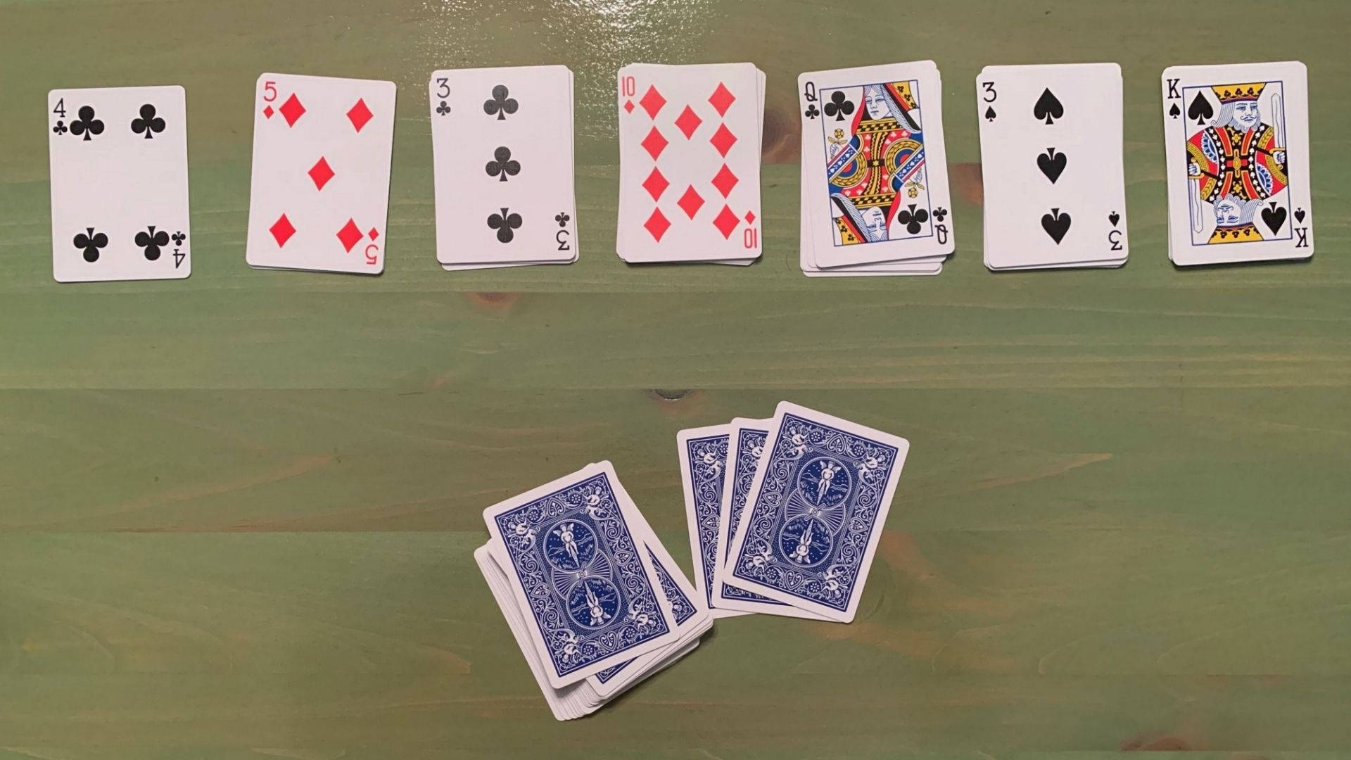 紙牌遊戲紙牌 壁紙 — 一排正面朝上的啤牌放在綠色木質表面上，附近有一小疊背面朝上的啤牌。