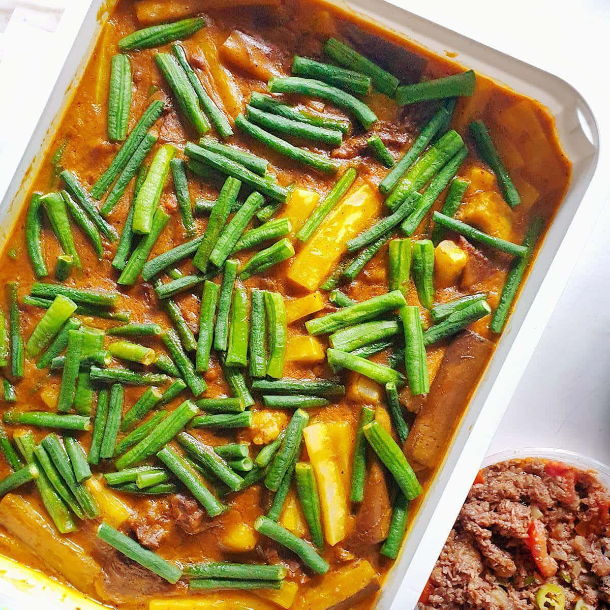 素食版菲律賓咖喱牛尾湯 壁紙 — 一個白色烤盤中，充滿活力的橙色咖喱配上綠色秋葵和黃色南瓜。
